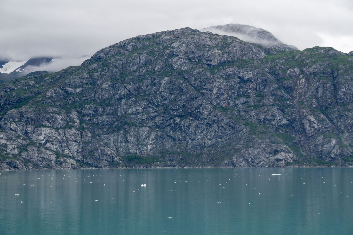 Towering granite cliffs rise from turquoise glacial waters dotted with small ice fragments.