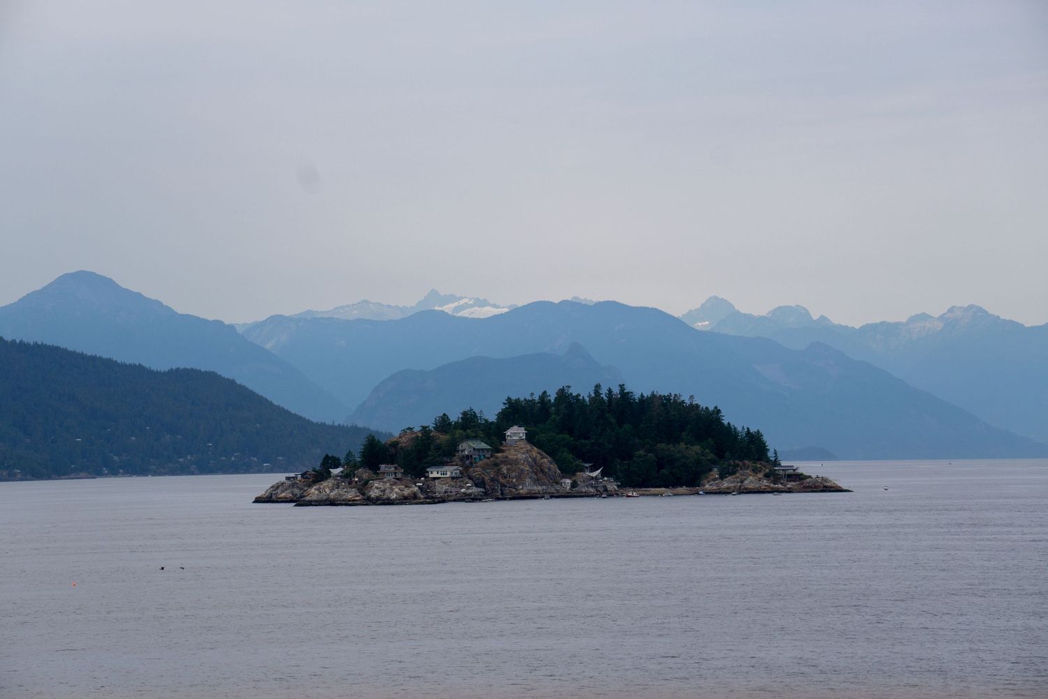 Small forested island surrounded by calm waters with mountain range in background.