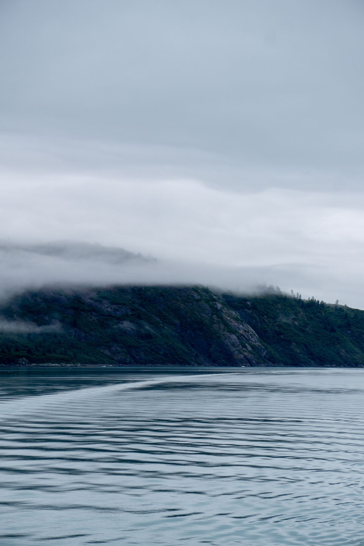 Dramatic mountain coastline with rippling waters and low-hanging fog creating a moody atmosphere.