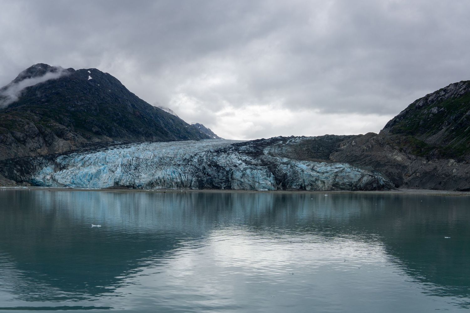 The blue ice face of a tidewater glacier reflects in the calm waters of an Alaskan bay.