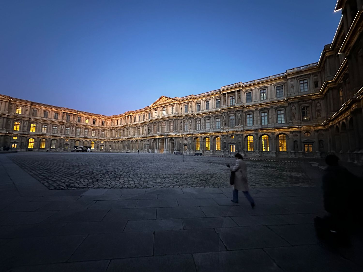 Historic courtyard with grand illuminated stone architecture at dusk with cobblestone plaza in golden evening light.