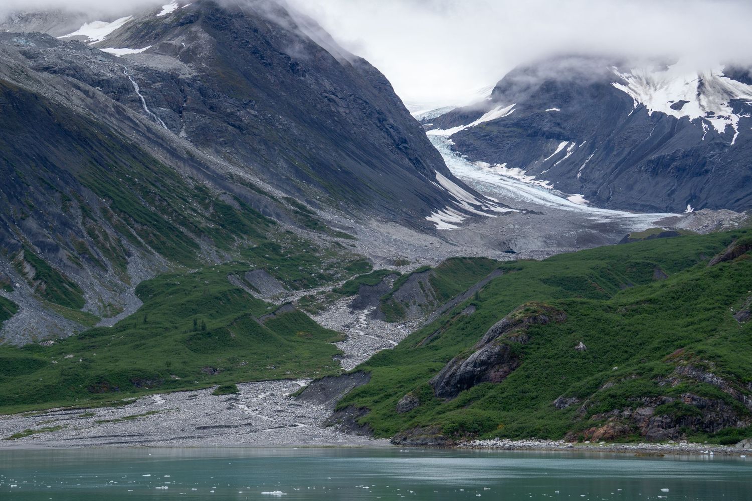 A glacier-carved valley with lush green slopes leads to snow-covered peaks in Alaska.
