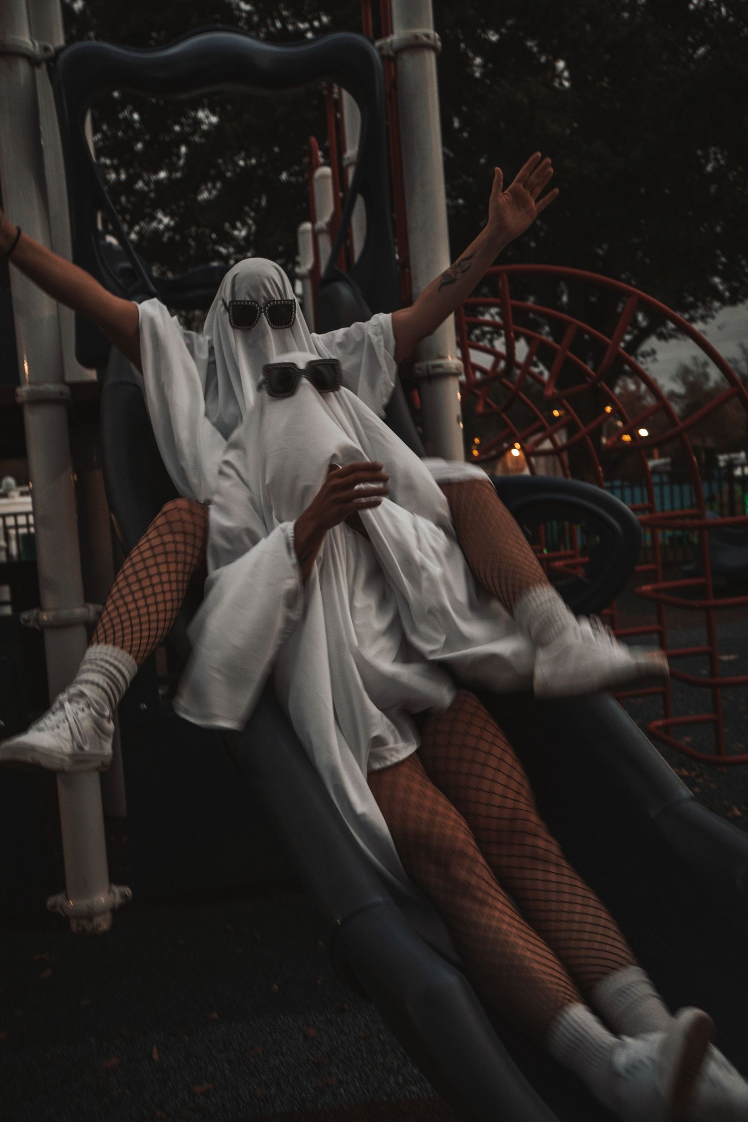 Person in white ghost Halloween costume sliding down playground slide.