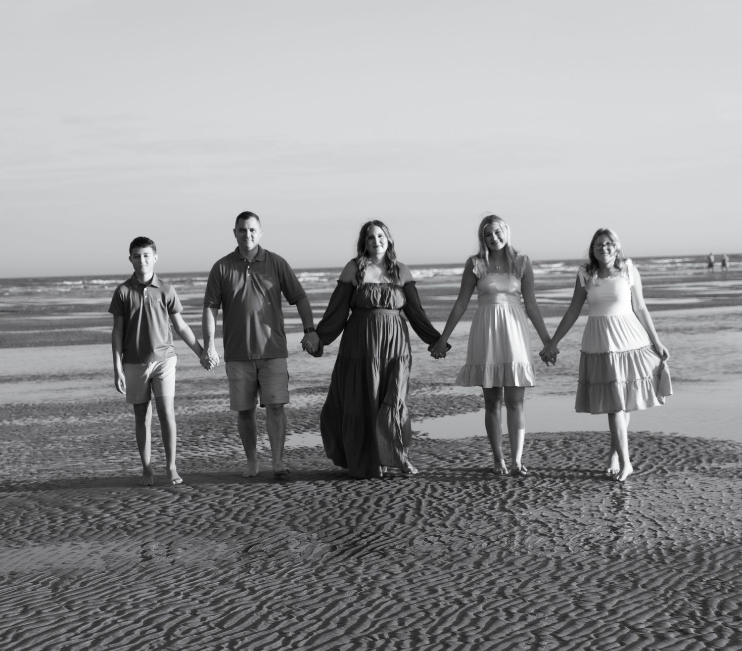 Black and white family photo of five people holding hands on a beach.