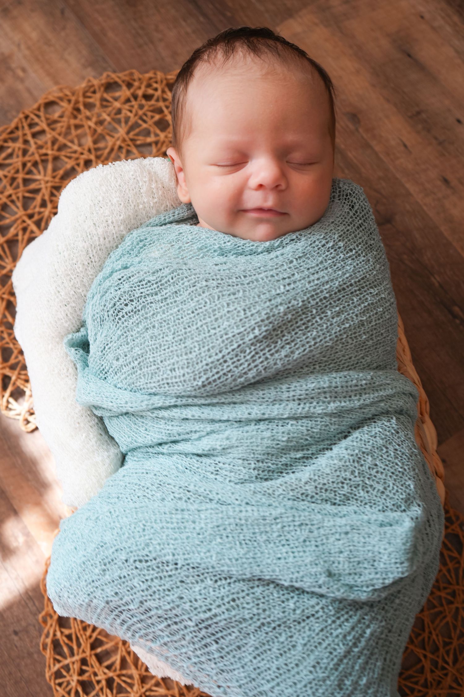 Serene newborn infant wrapped snugly in a light blue knit blanket resting in a wicker basket, smiling softly.