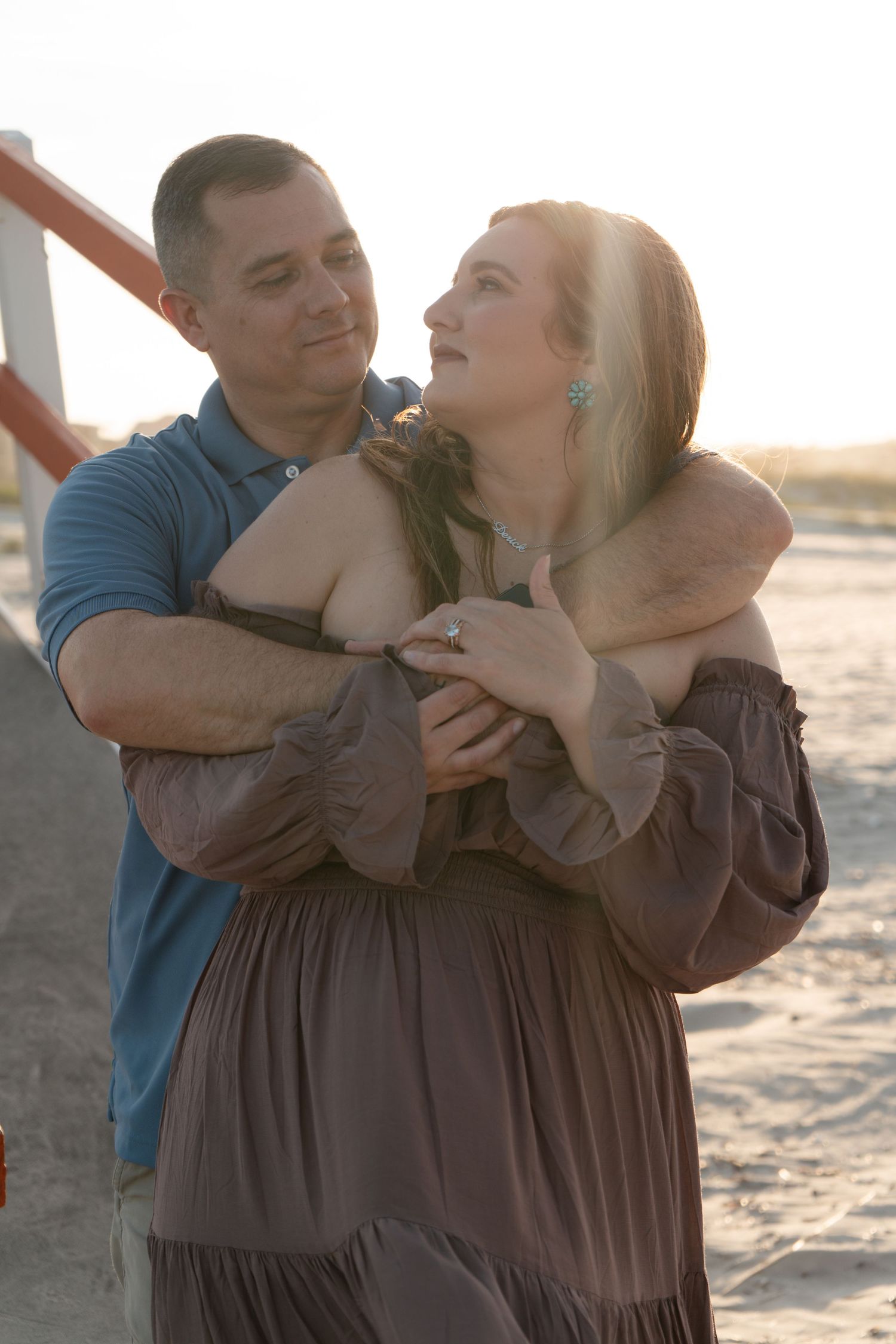 A couple embracing and smiling at each other on a beach at golden hour sunset.