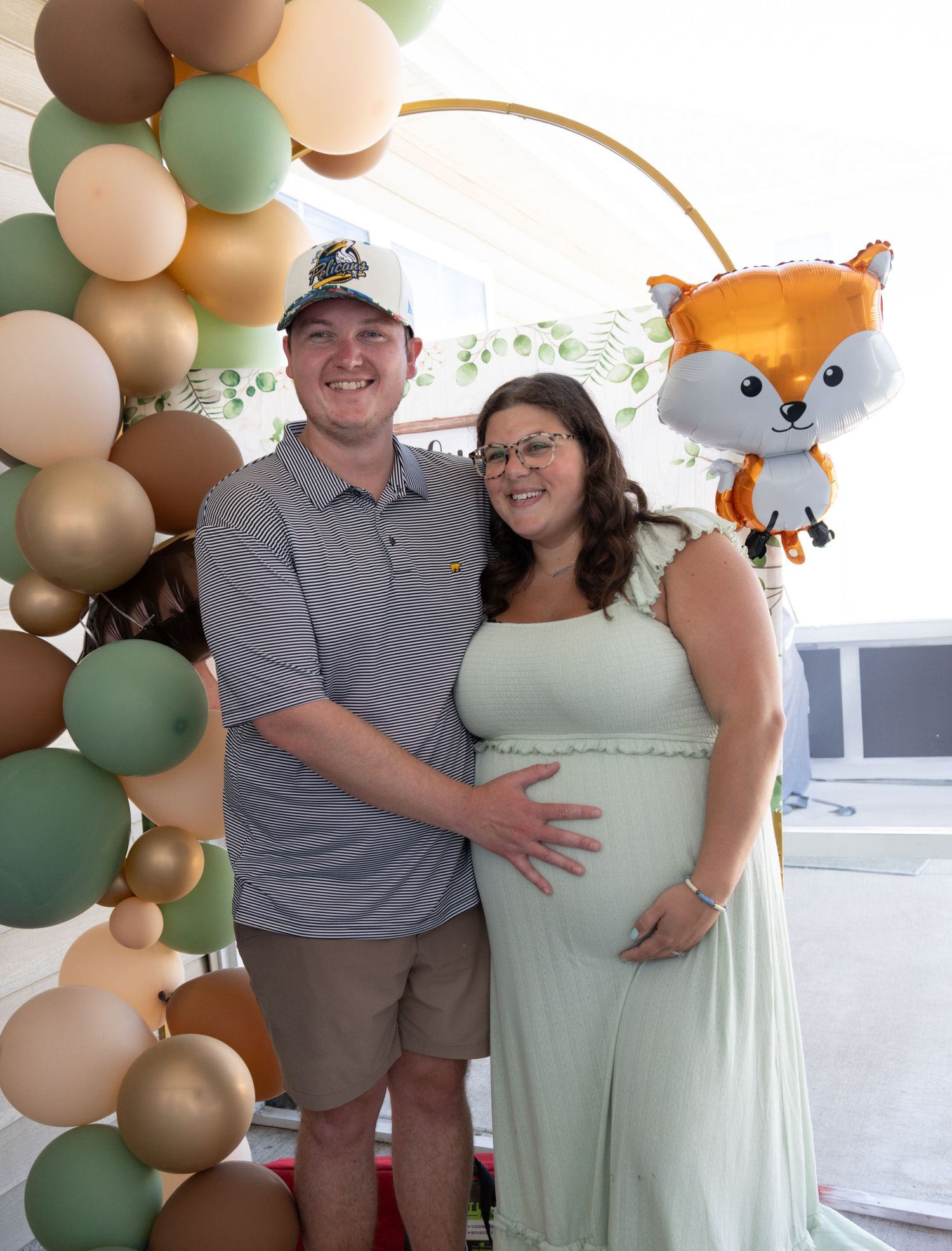 Pregnant woman in mint dress with partner at fox-themed baby shower with balloon arch.