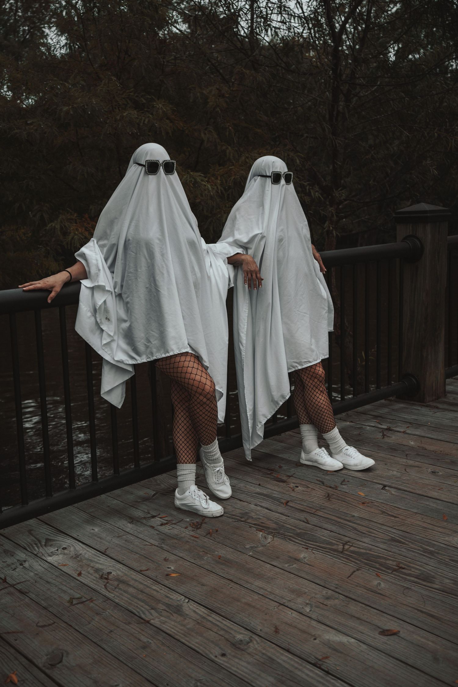 Two people in white ghost costumes with sunglasses posing on wooden deck.