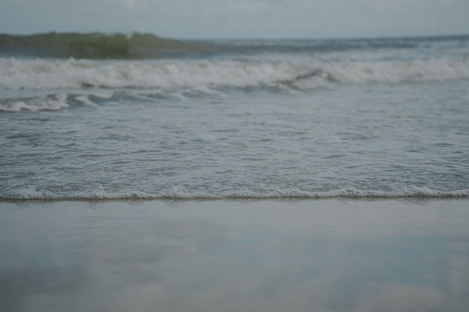 Gentle ocean waves washing onto sandy beach shore with calm blue water.