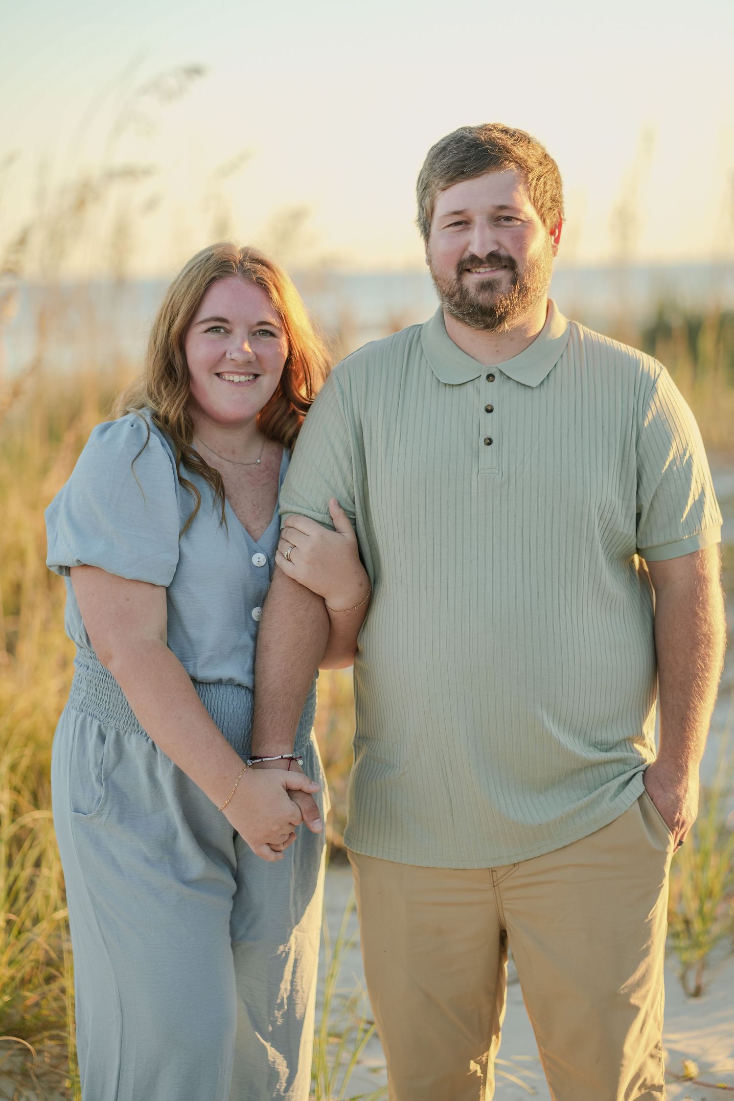 Smiling couple in coordinating sage green outfits posing at golden hour beach.