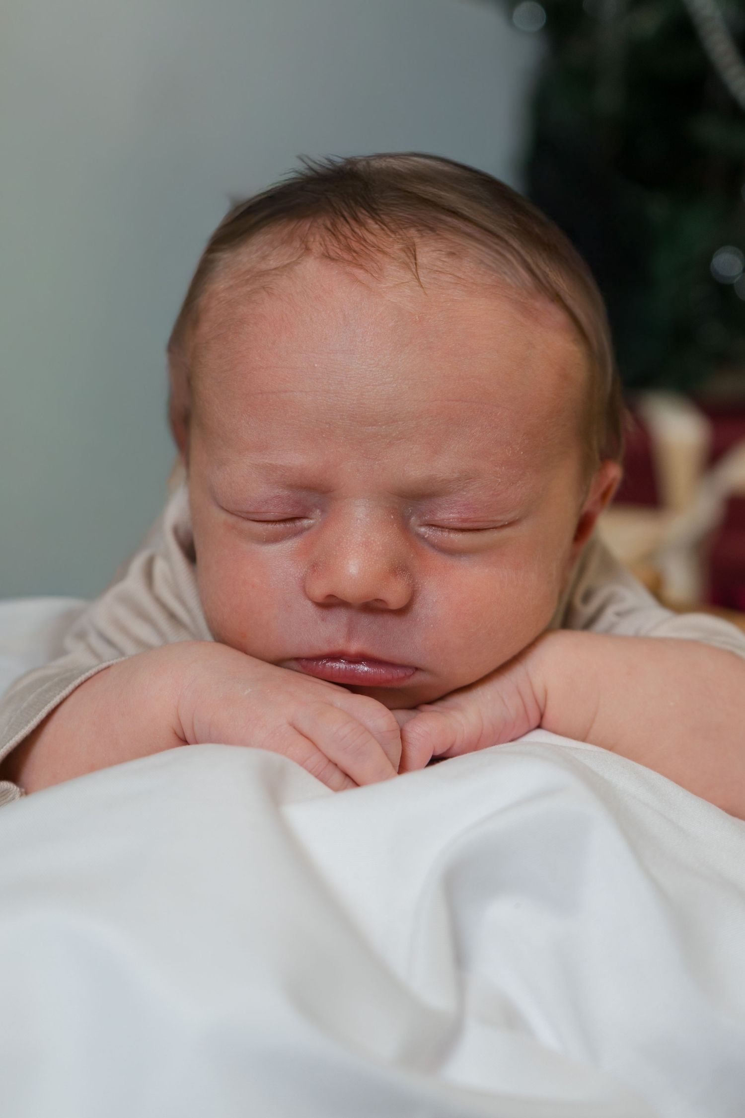 A peaceful newborn baby sleeps with chin resting on folded hands atop white blanket.