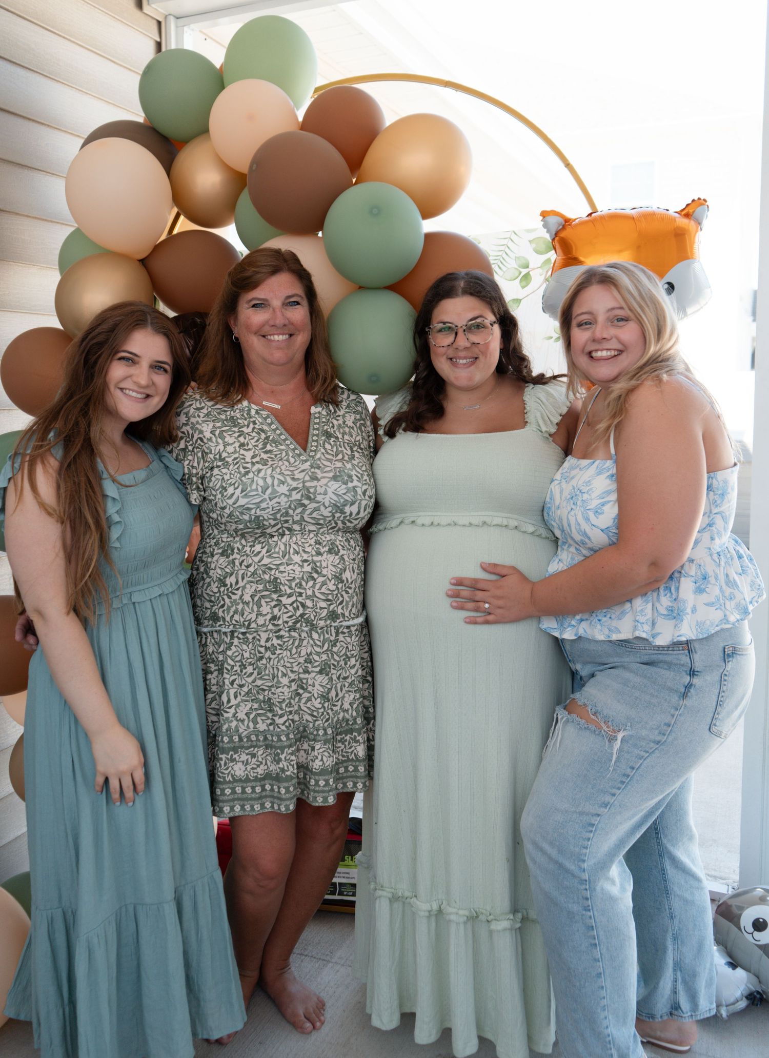 Pregnant woman in mint dress poses with three women at woodland-themed baby shower.