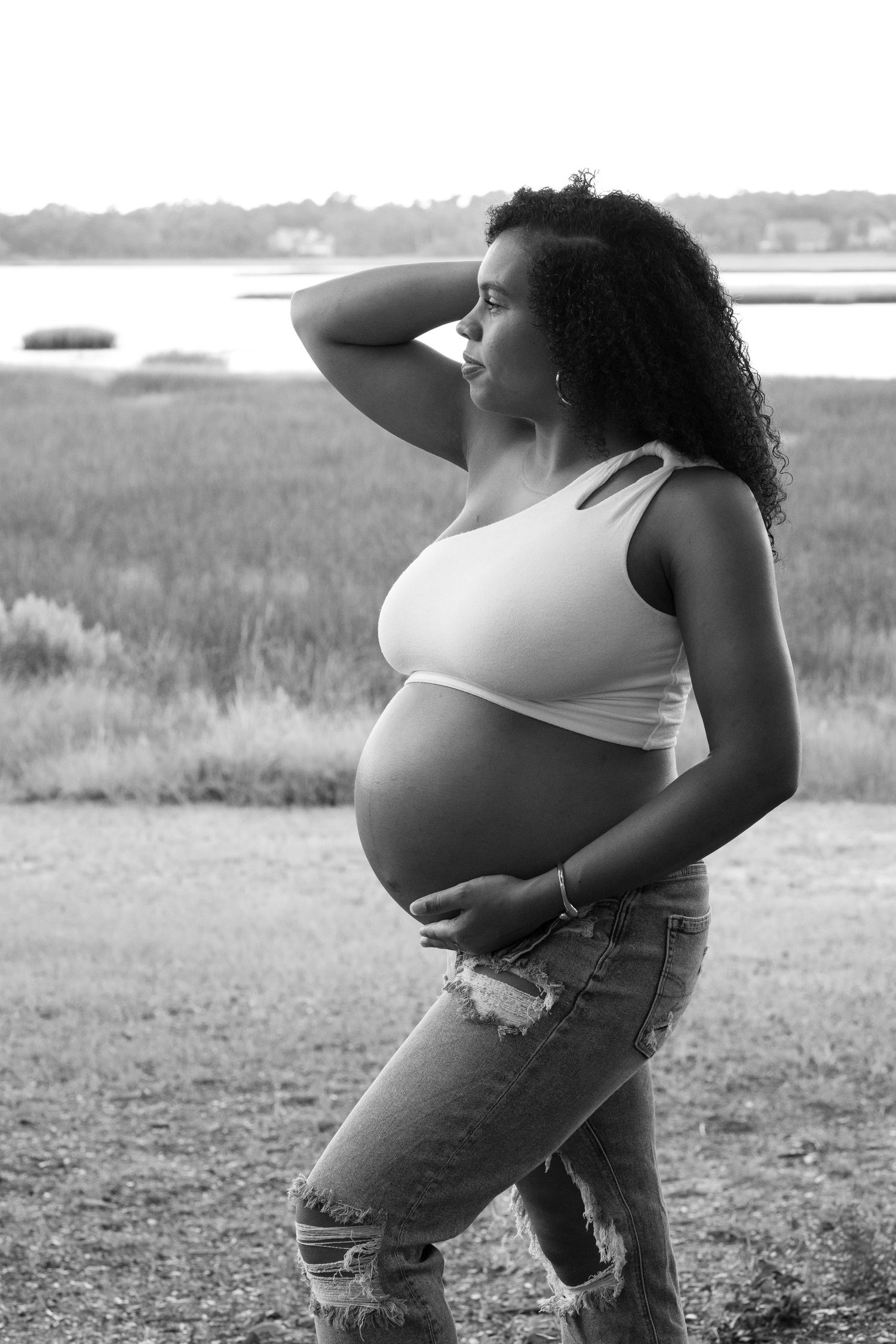 Black and white portrait of pregnant woman in white top and jeans near marsh.
