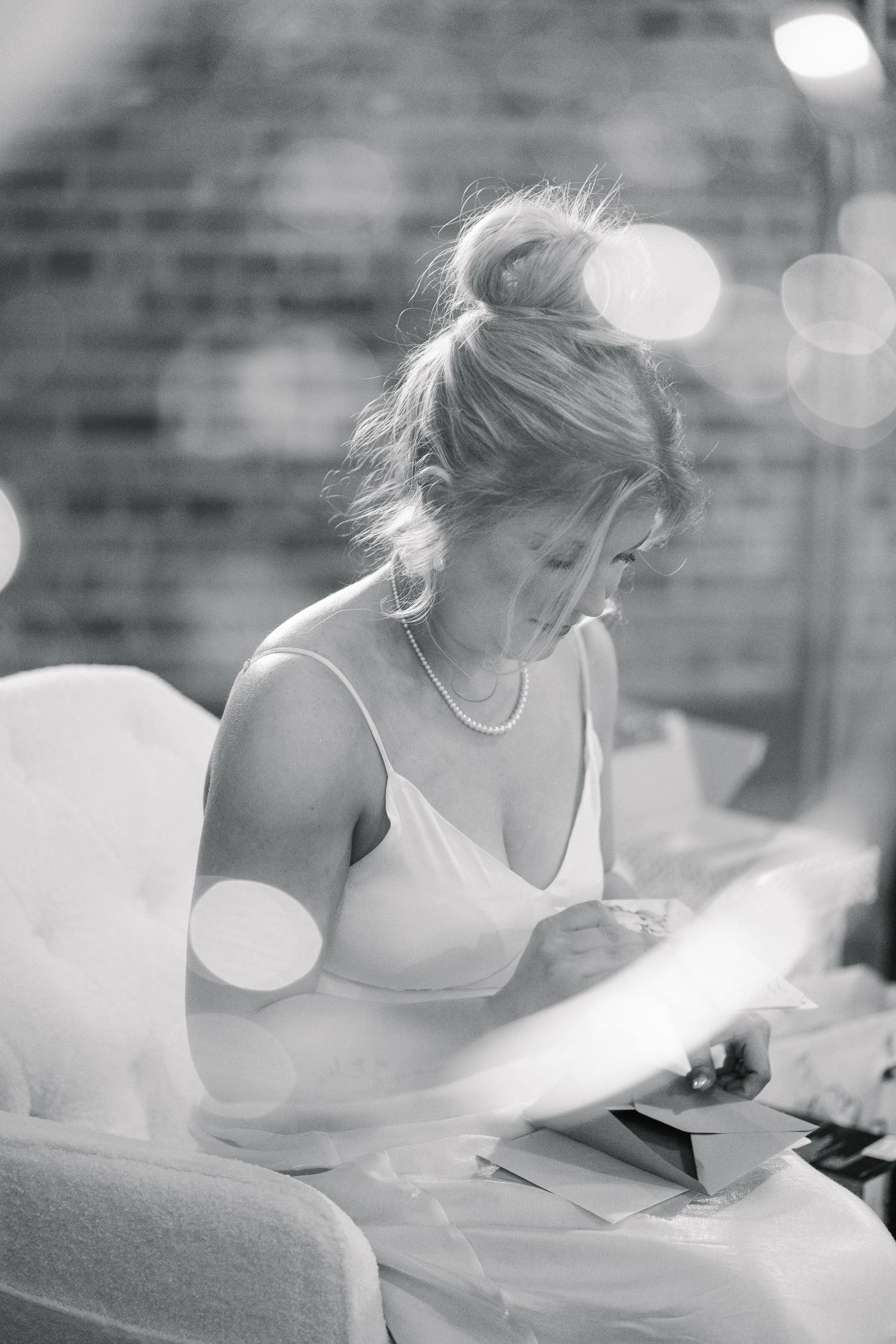 Bride in white slip dress reading a letter while seated, black and white bridal shower photo.