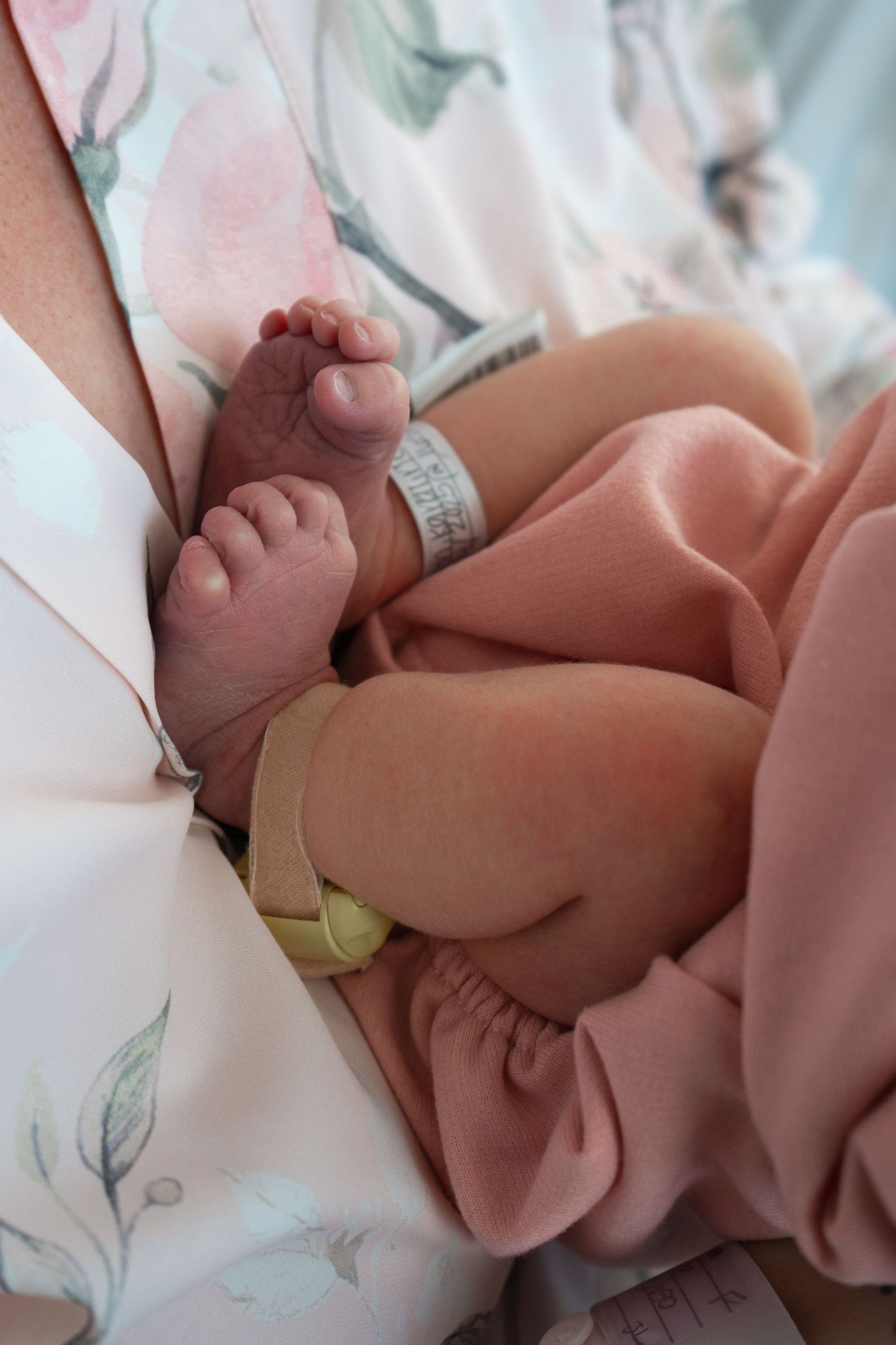 Close-up of newborn baby feet with hospital ID bracelet wrapped in pink blanket on mothers lap.