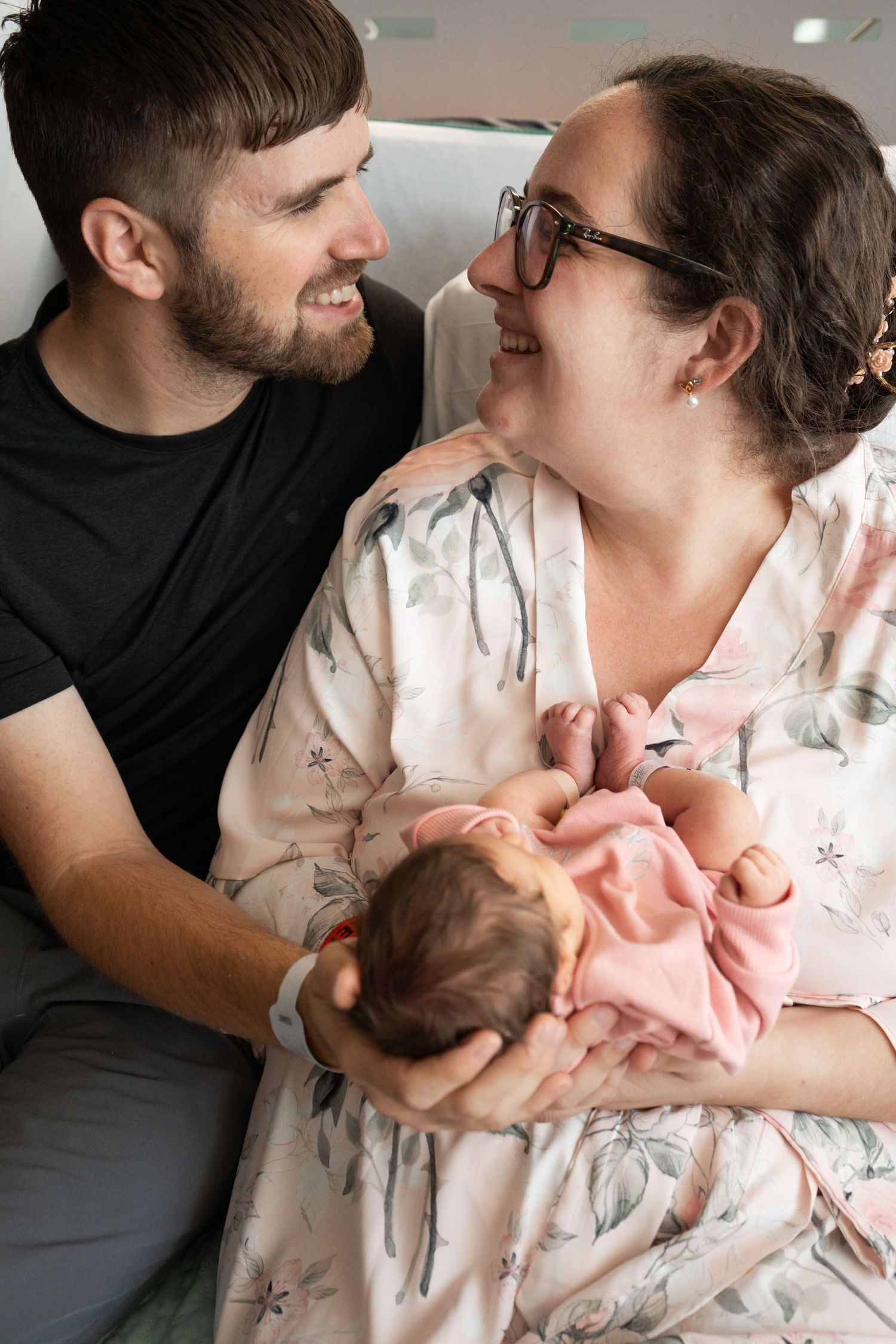 Happy new parents smiling at each other while holding newborn baby in hospital.