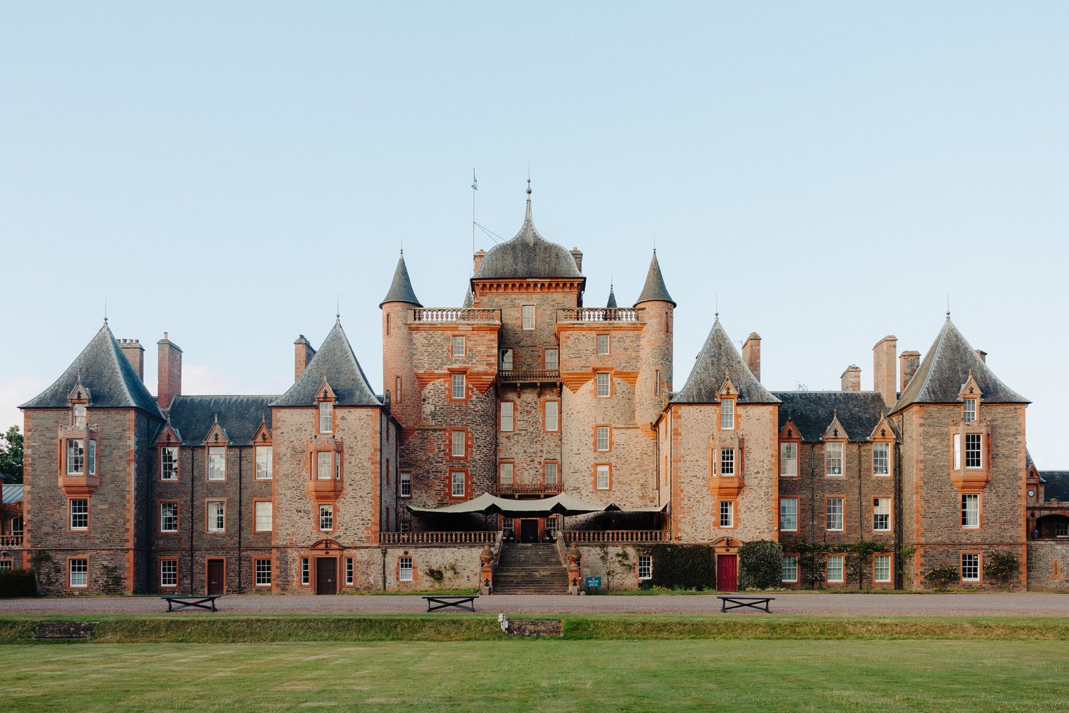 Historic Scottish castle with turrets and stone facade surrounded by green lawn under clear blue sky.