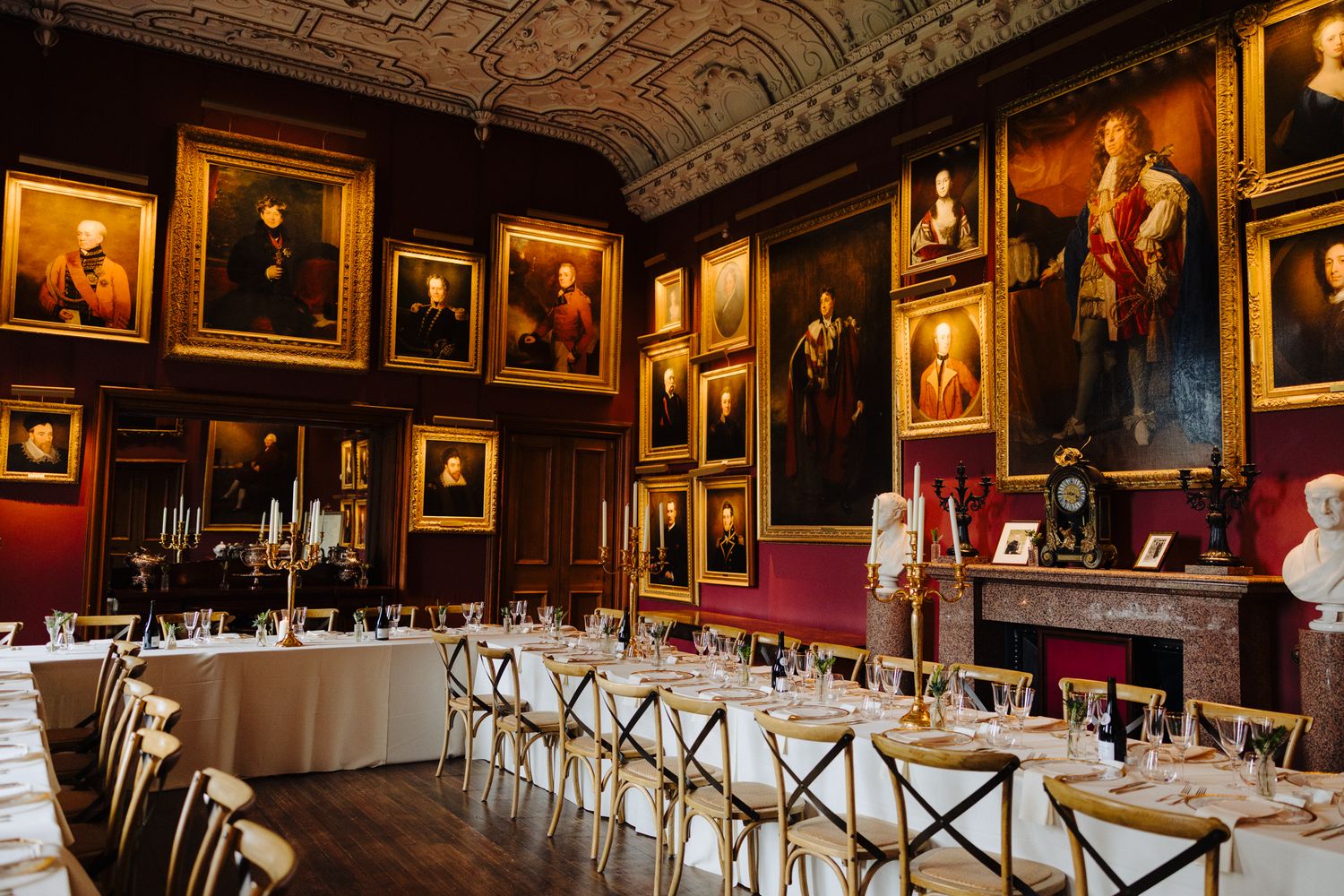 Elegant dining room with gold-framed portraits, long banquet table set for dinner, candelabras, and ornate fireplace.
