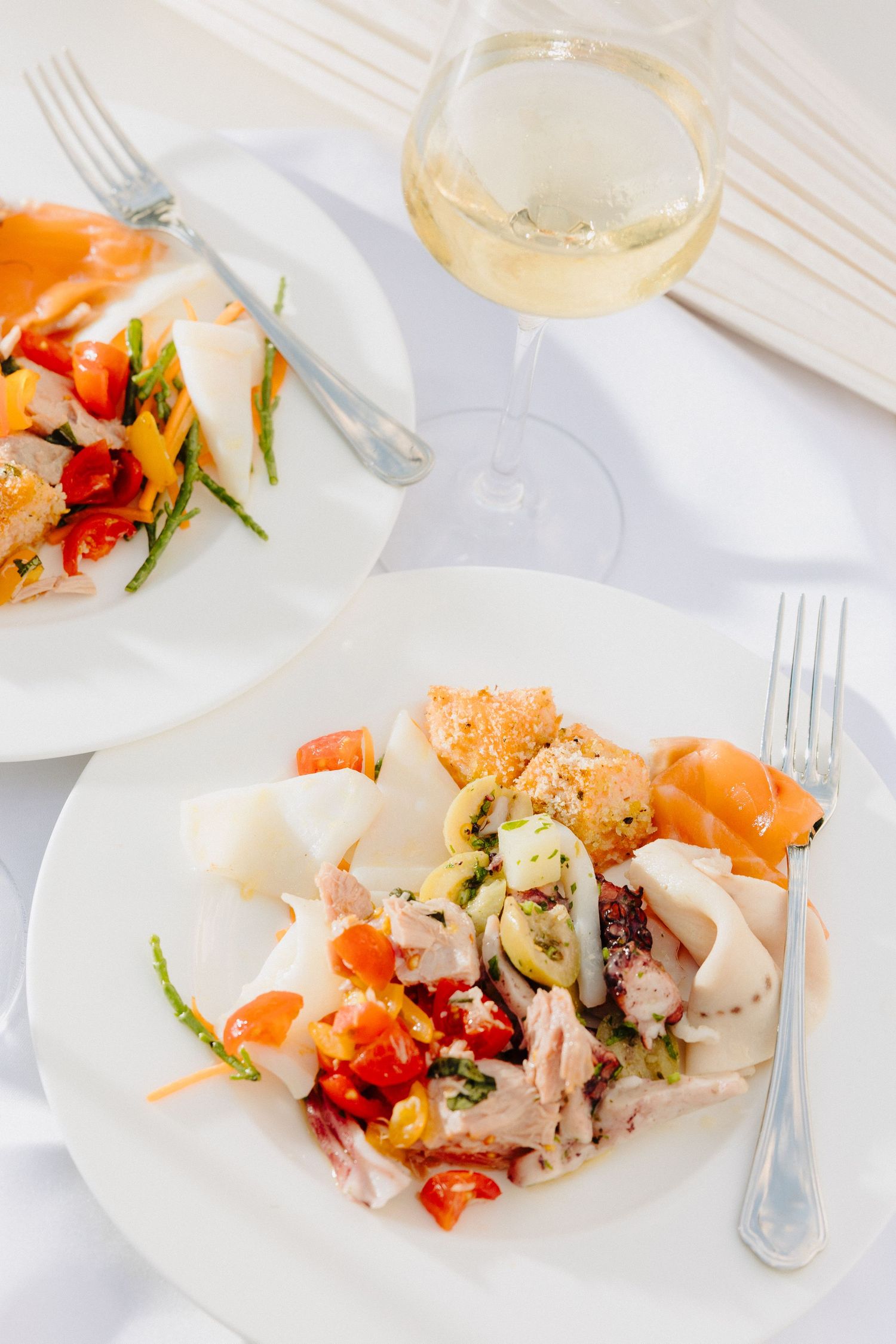 Elegant seafood salad with tomatoes, calamari, and fresh vegetables served on white plates with white wine at a wedding.