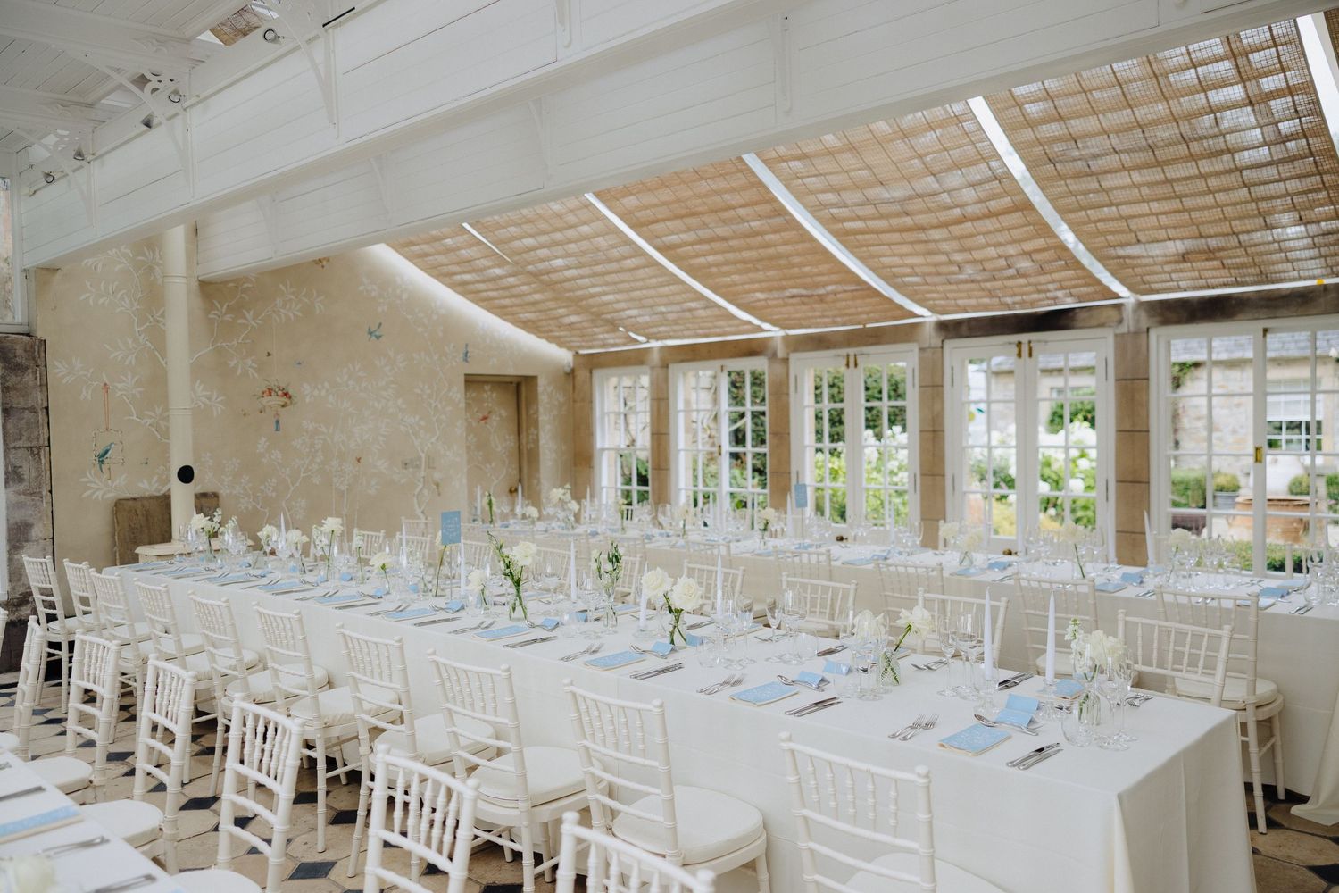 Elegant wedding reception hall with long white tables, chiavari chairs, and a glass ceiling in a stone venue.