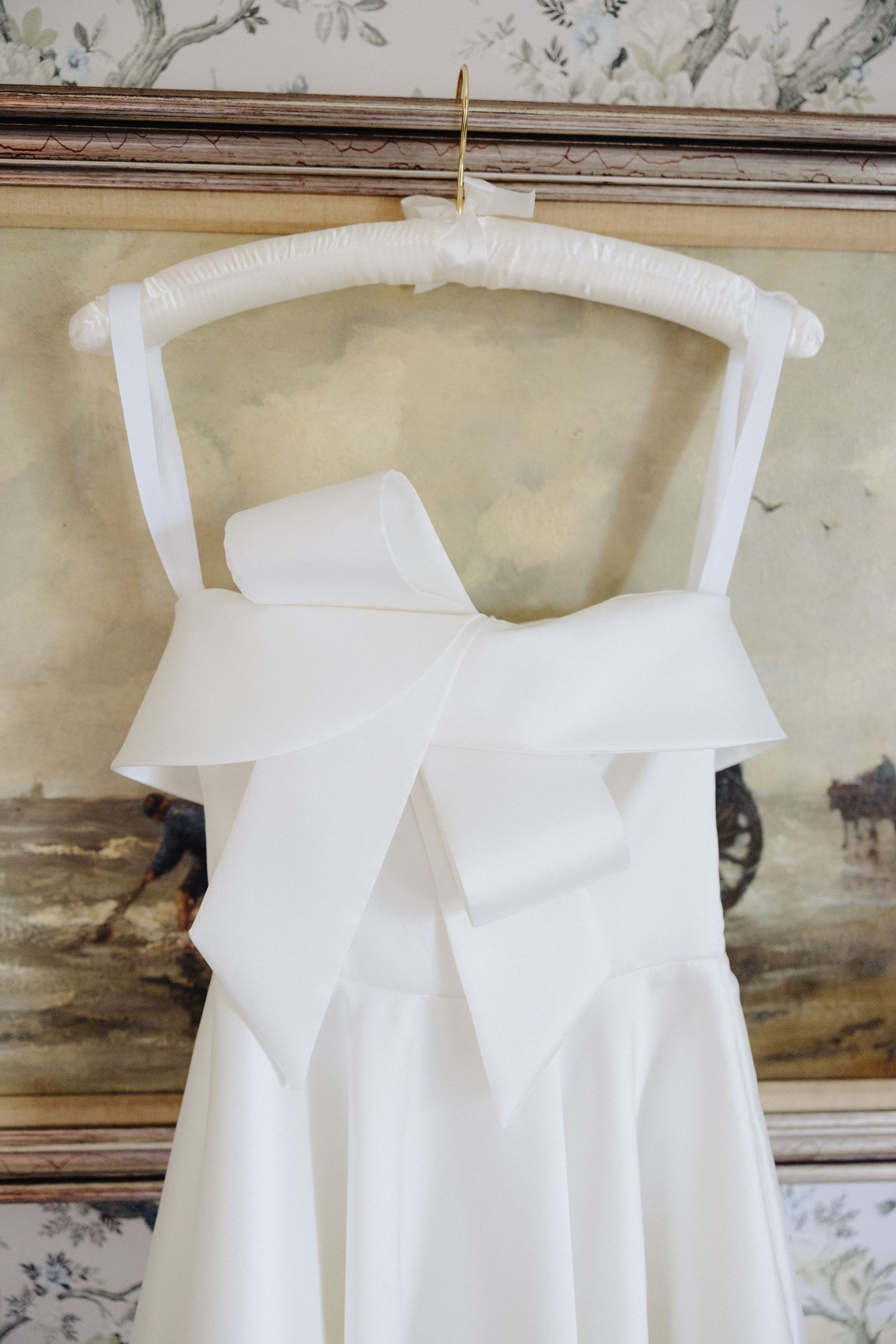 White wedding dress with large satin bow detail hanging on padded hanger.