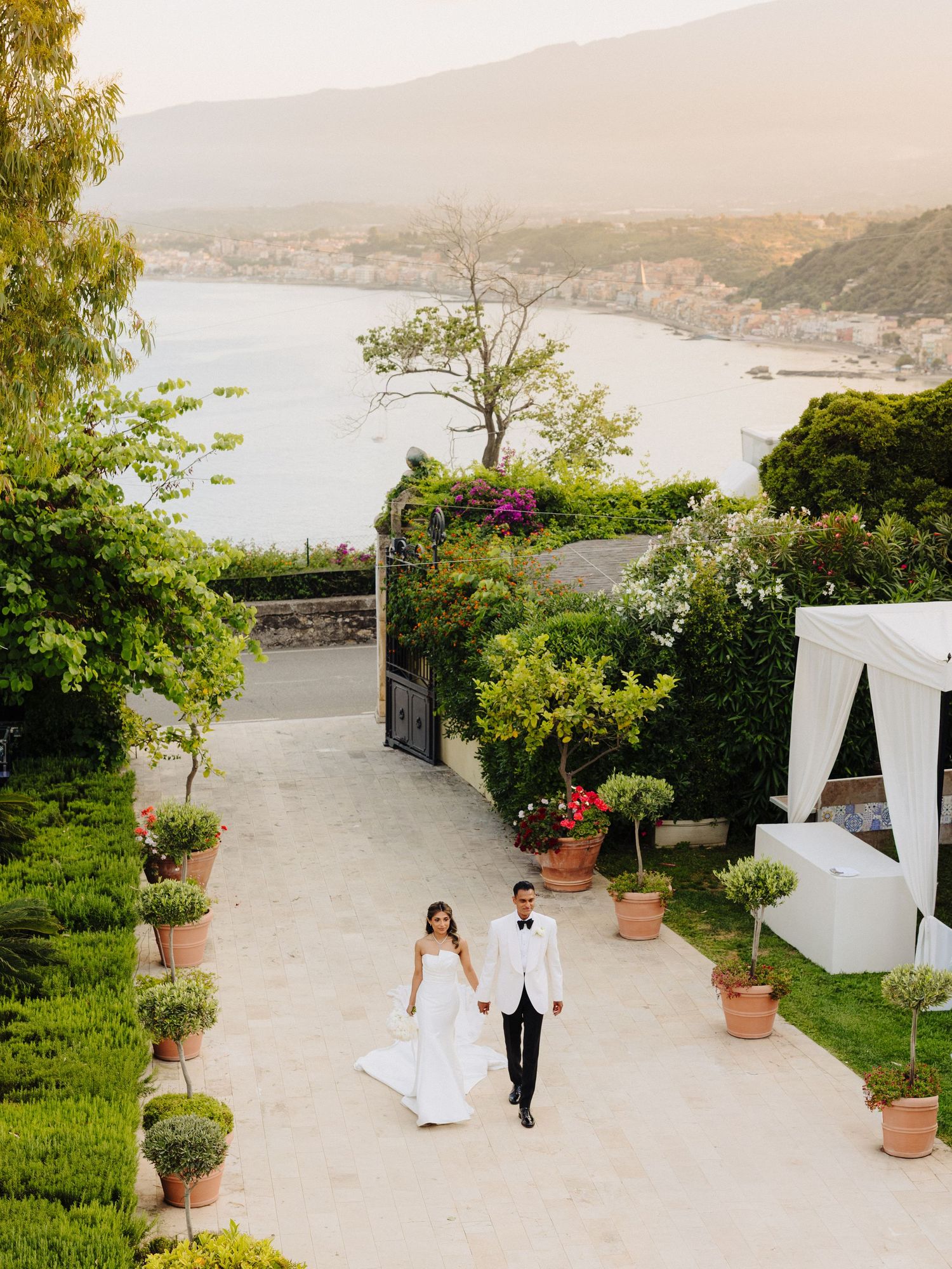 Bride and groom walking hand-in-hand on a scenic coastal wedding venue terrace with stunning sea views in Italy.