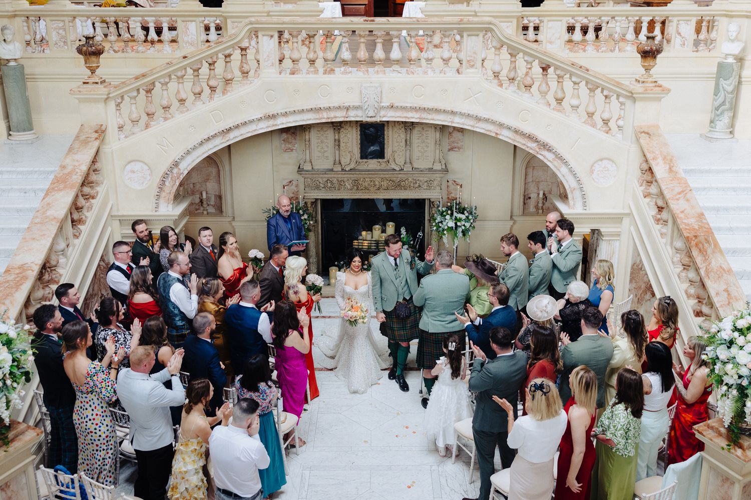 Elegant wedding ceremony on grand marble staircase with guests gathered around bride and groom in ornate venue.