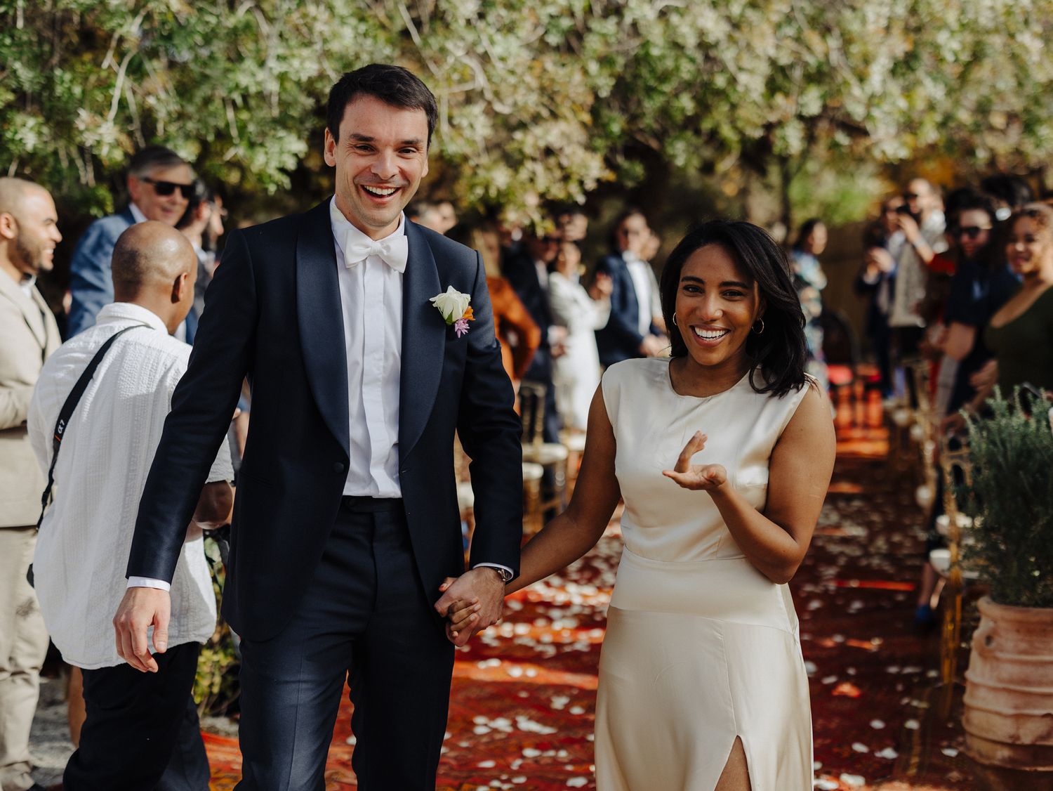 Happy newlyweds walk hand-in-hand at an outdoor garden wedding ceremony, surrounded by cheering guests.