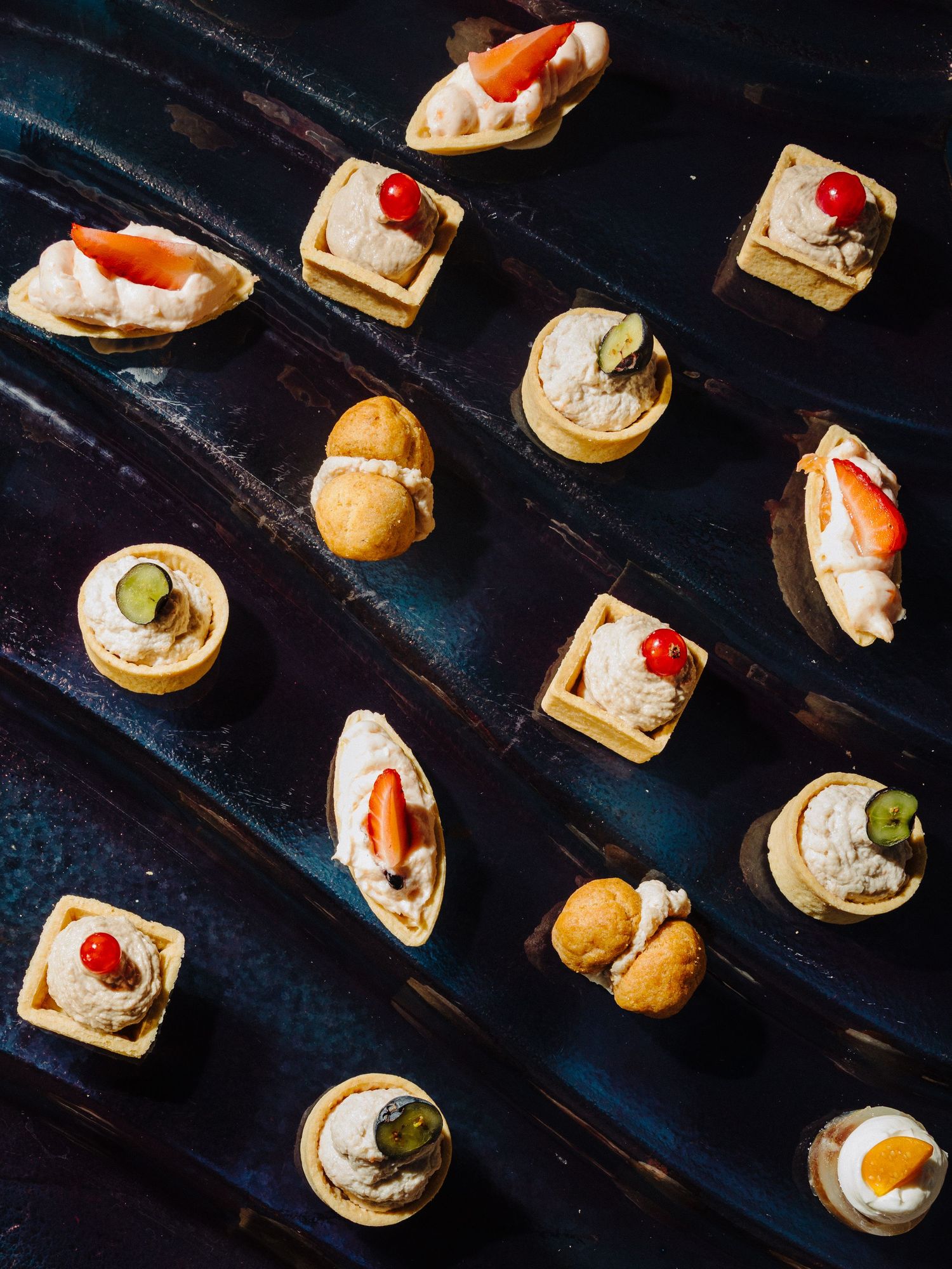 Elegant assortment of gourmet canapes and bite-sized appetizers arranged on dark slate serving board.