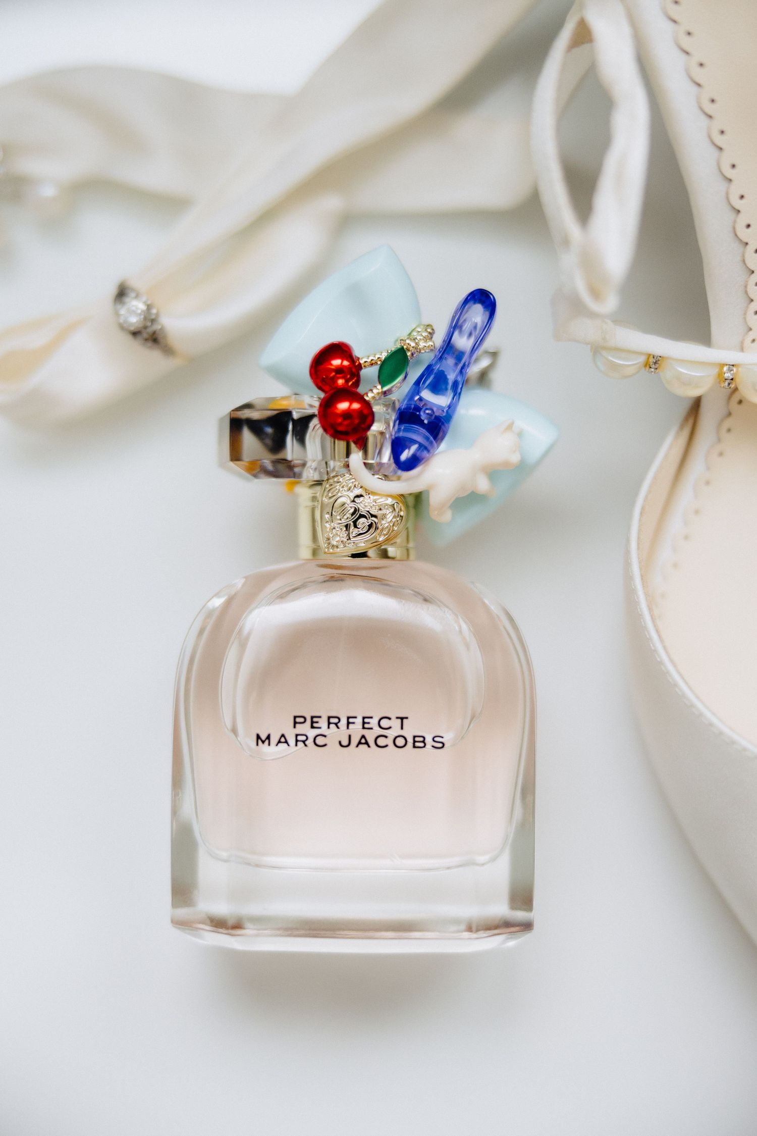Perfect Marc Jacobs perfume bottle with decorative cherry and bow cap beside bridal accessories.