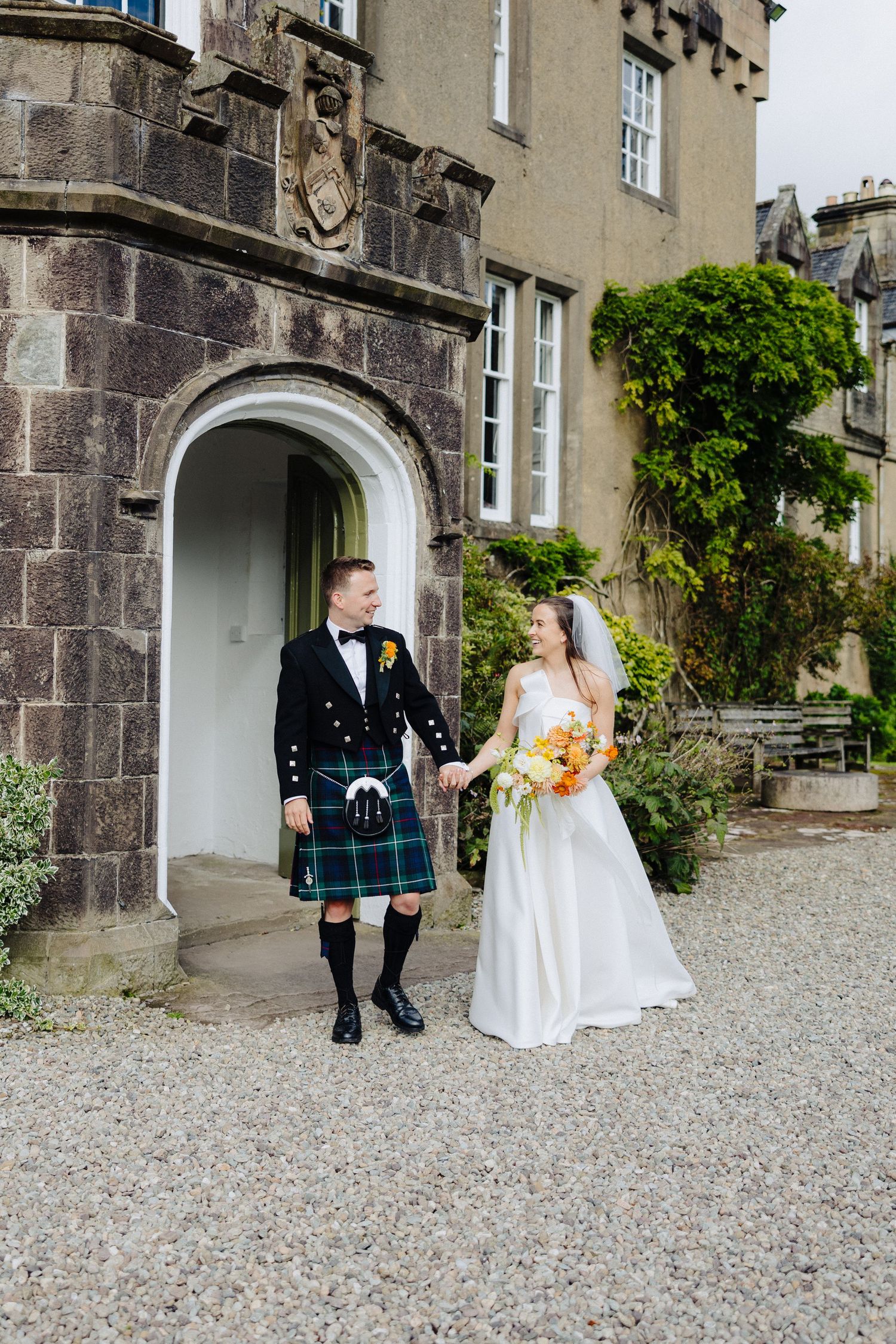 Bride and groom in tartan kilt holding hands outside a Scottish castle venue.