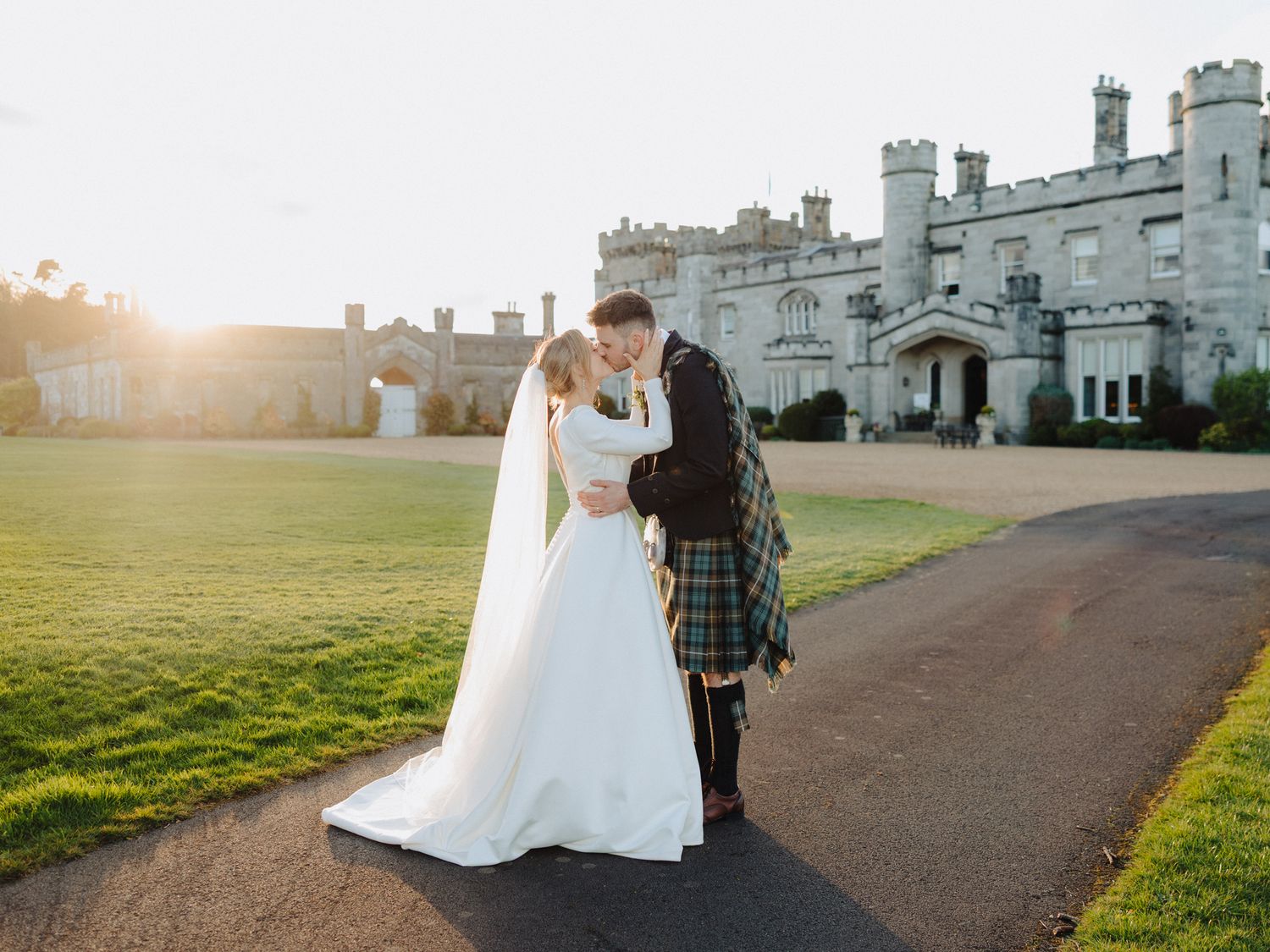 Bride and groom sharing a romantic kiss at golden hour outside a stunning Scottish castle wedding venue.