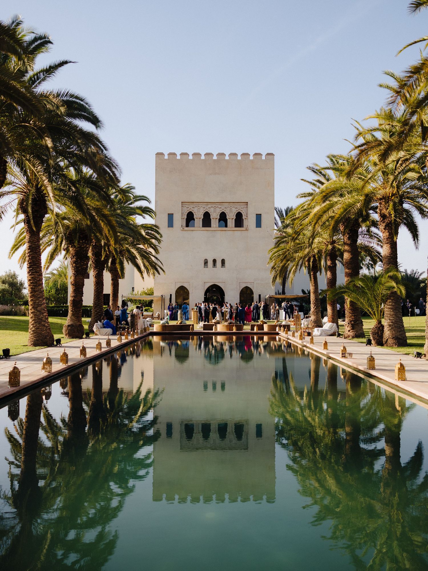 Stunning Moroccan wedding venue with a reflective pool lined with palm trees and a white tower.