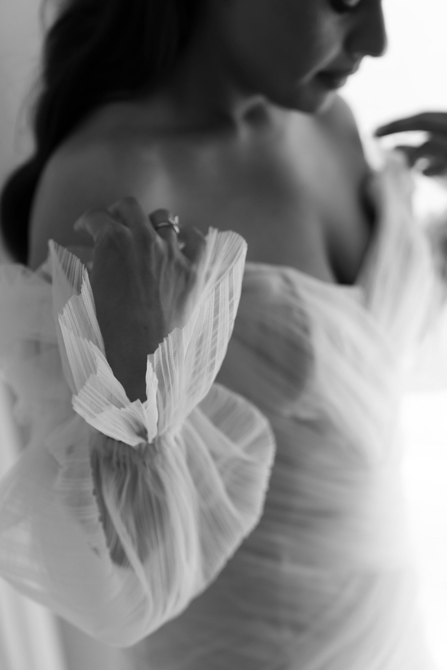 Black and white close-up of a bride in a sheer tulle off-shoulder wedding gown with ruffled sleeves.