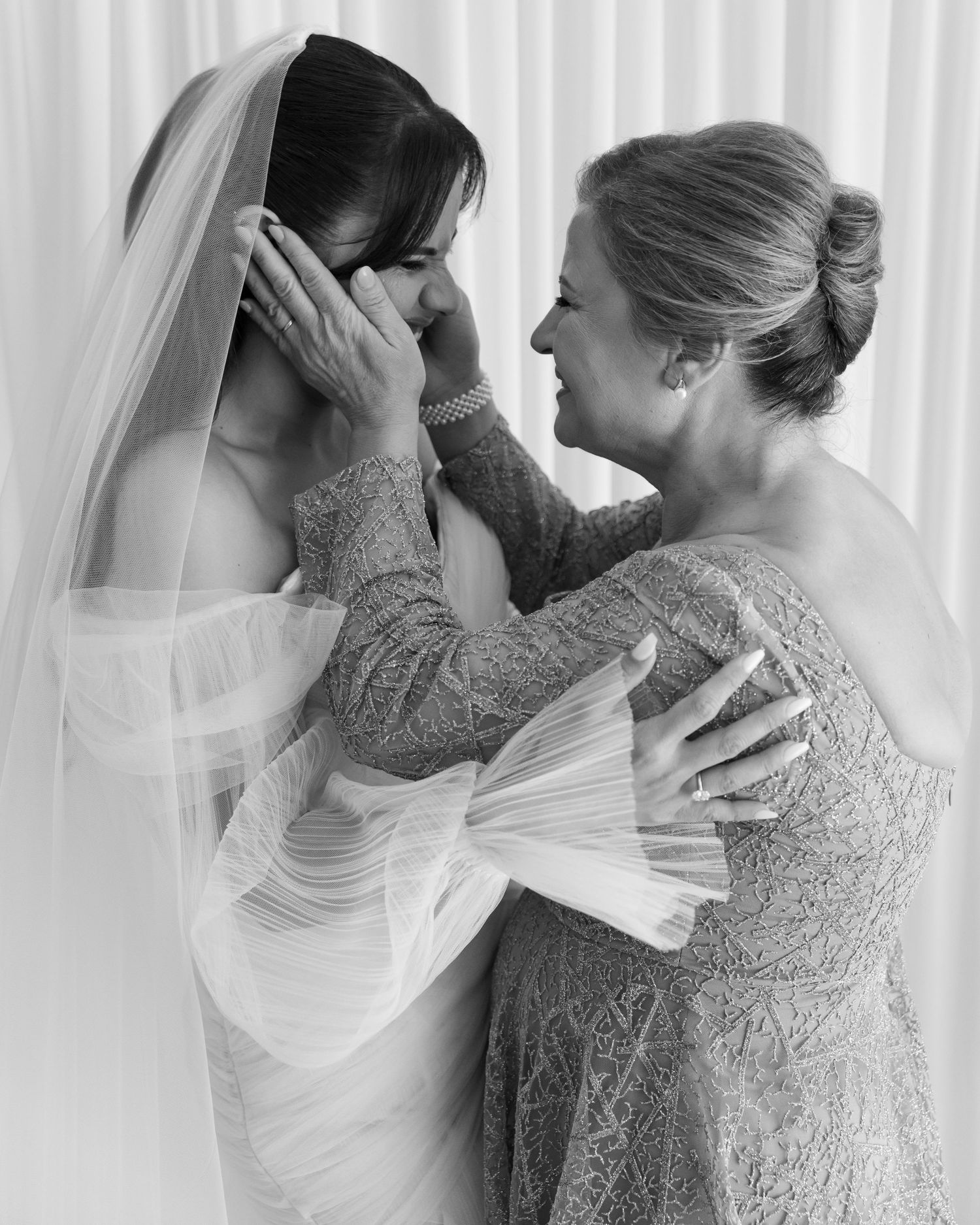 Mother tenderly adjusts brides veil in an emotional black and white wedding preparation portrait.