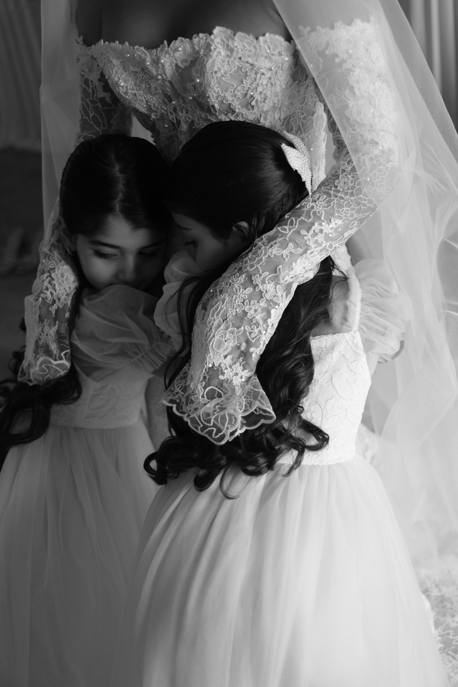 Black and white photo of a bride embracing two young flower girls in white dresses.