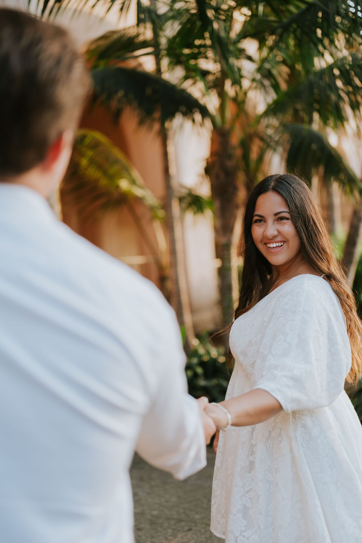 Joyful couple in white clothing dancing and twirling under palm trees.