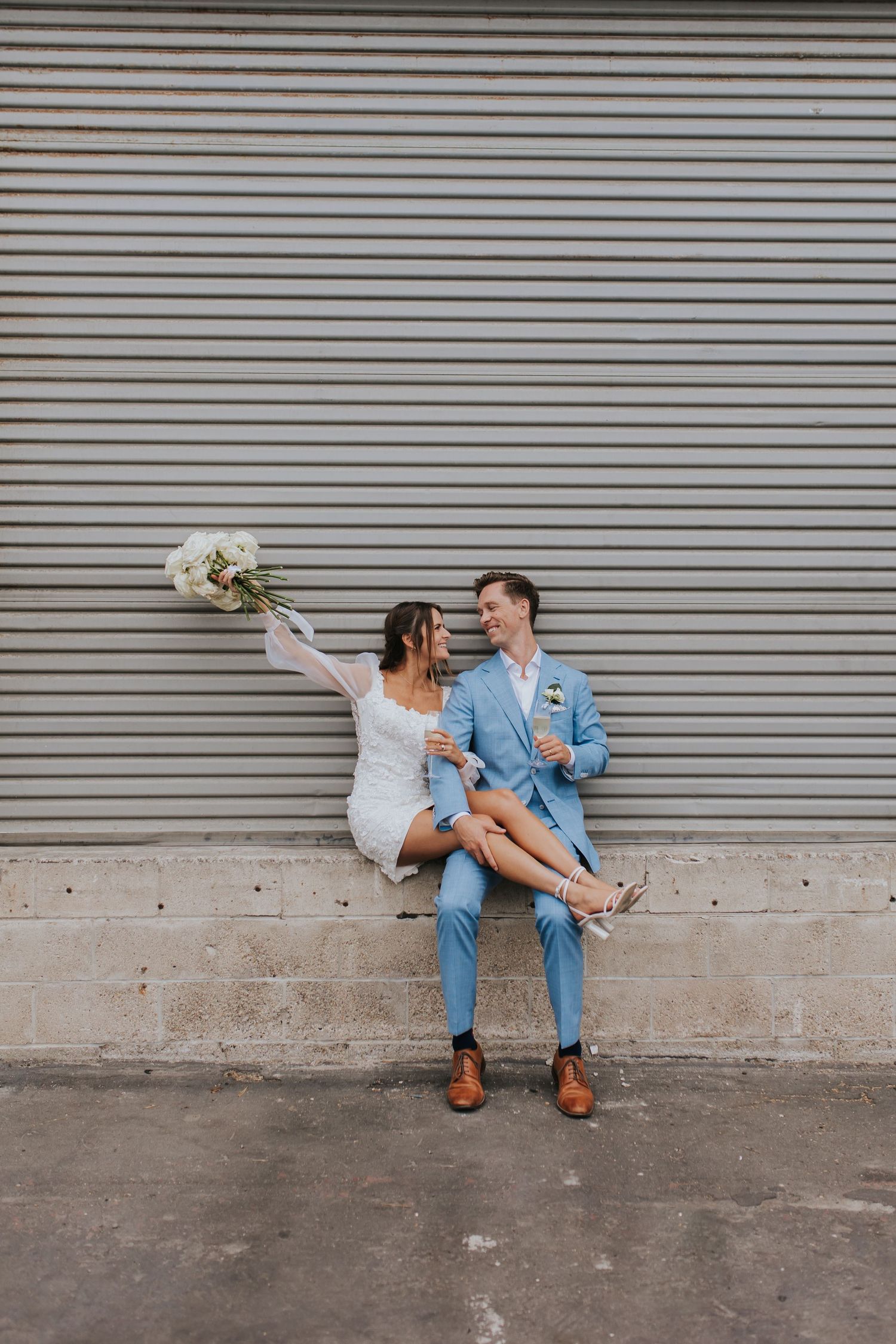 A creative wedding photo series showing a couple sitting and posing playfully against an industrial backdrop.