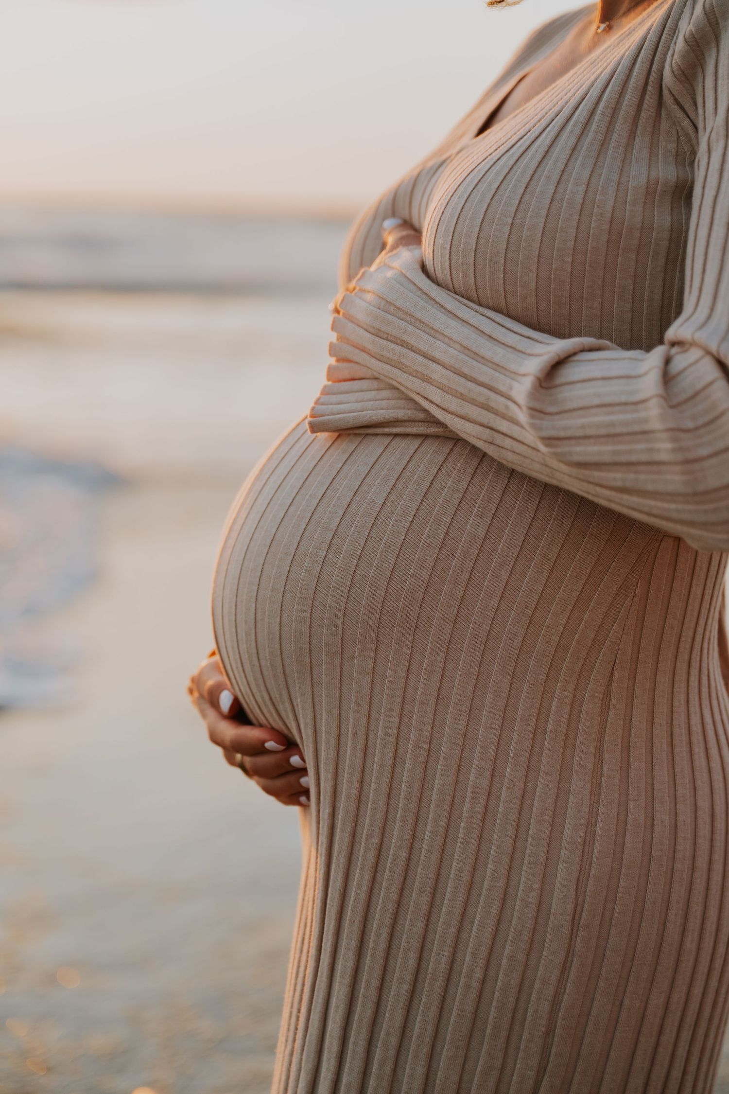 Close-up shots of maternity sweater showing pregnancy bump against beach backdrop.