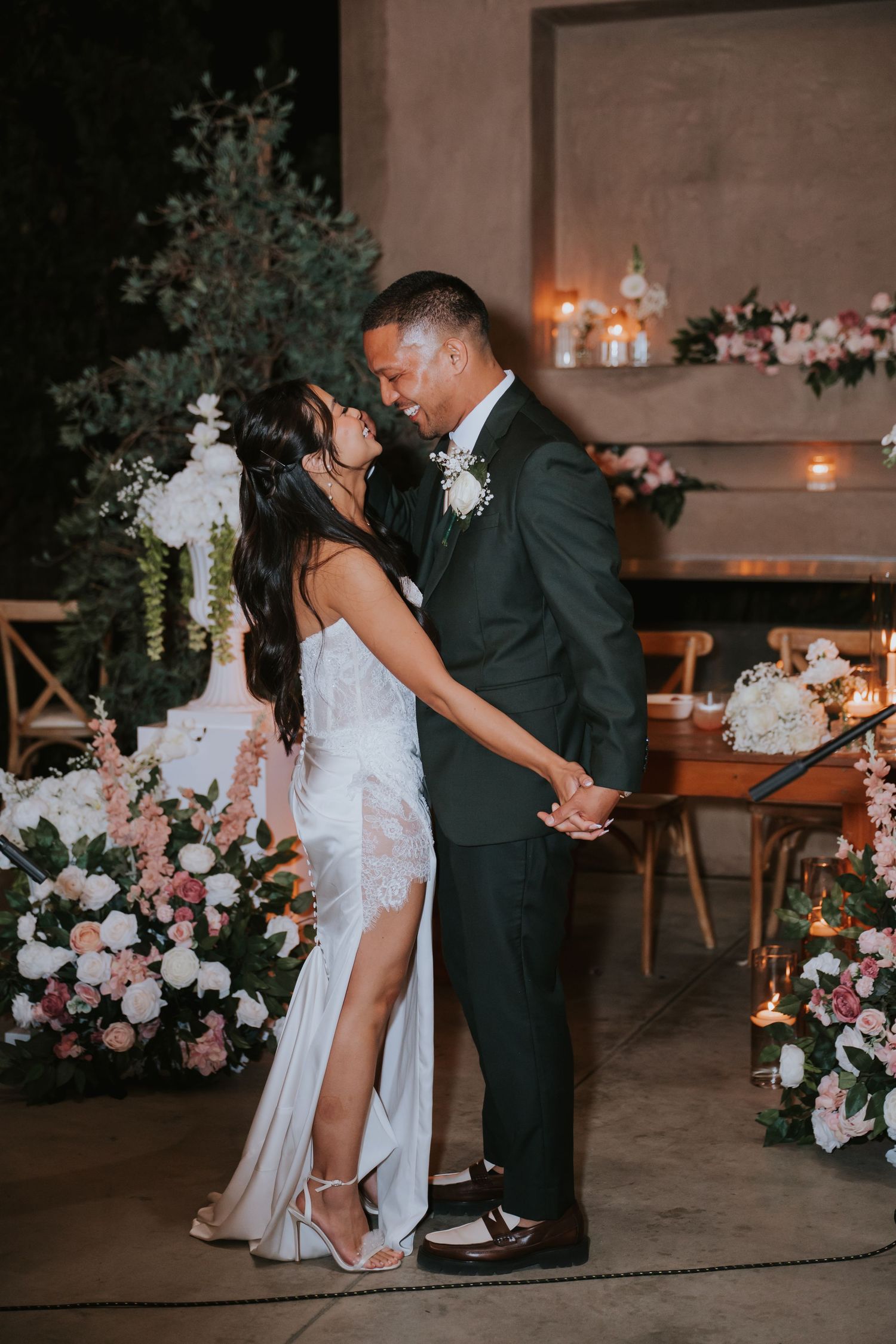 A romantic first dance moment at a wedding reception decorated with pink and white floral arrangements and candlelight.