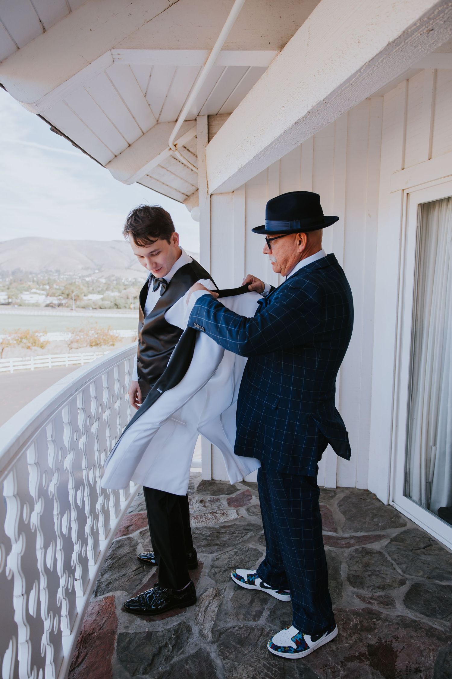 Wedding couple dances playfully on a white balcony with ocean views.