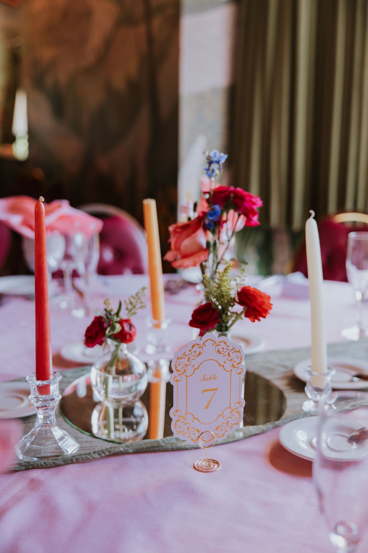 Elegant wedding reception table setting with pink linens, red candles, and delicate floral centerpieces.