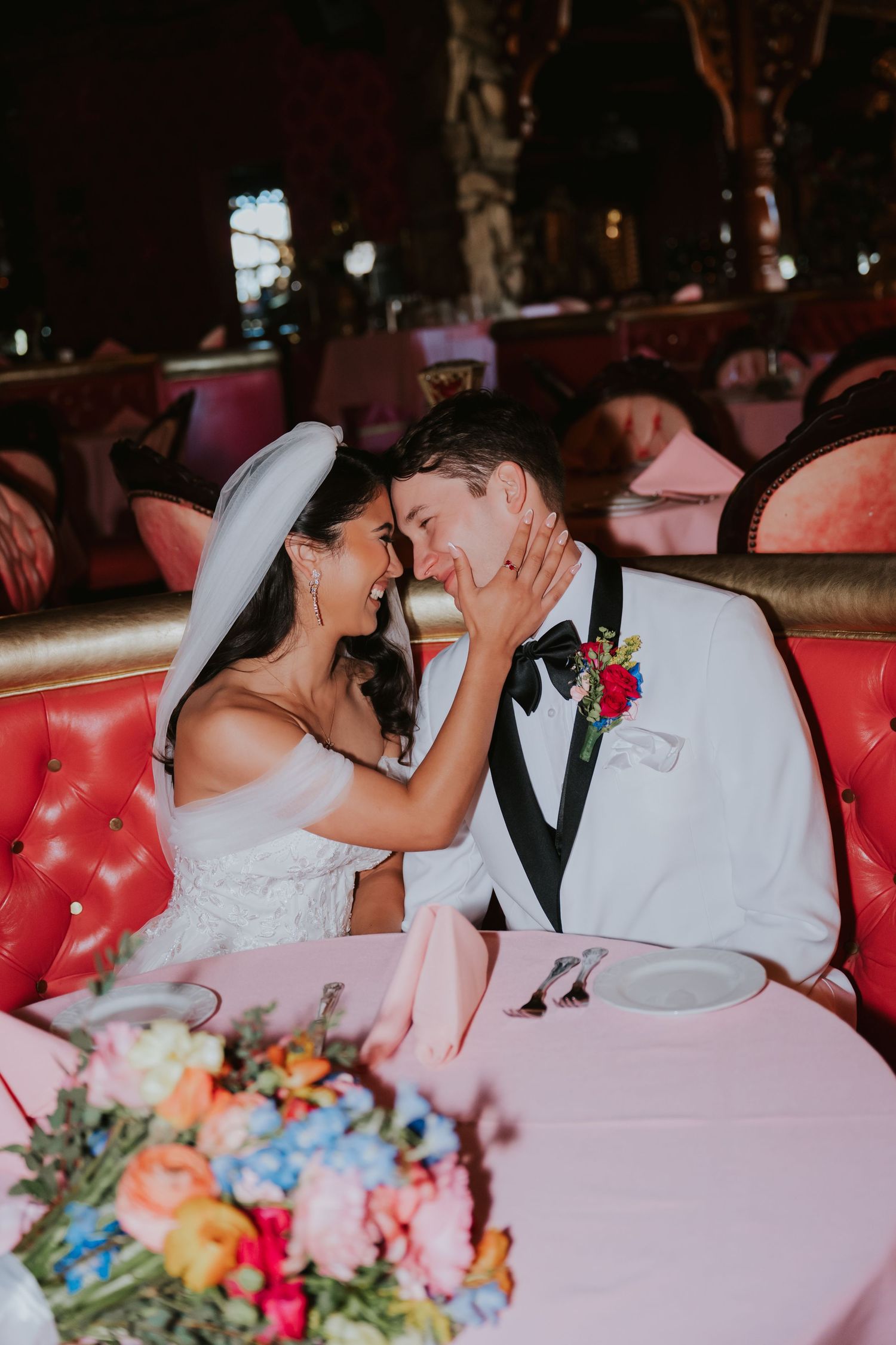 A romantic moment between newlyweds on a red leather couch with colorful flowers in the foreground.