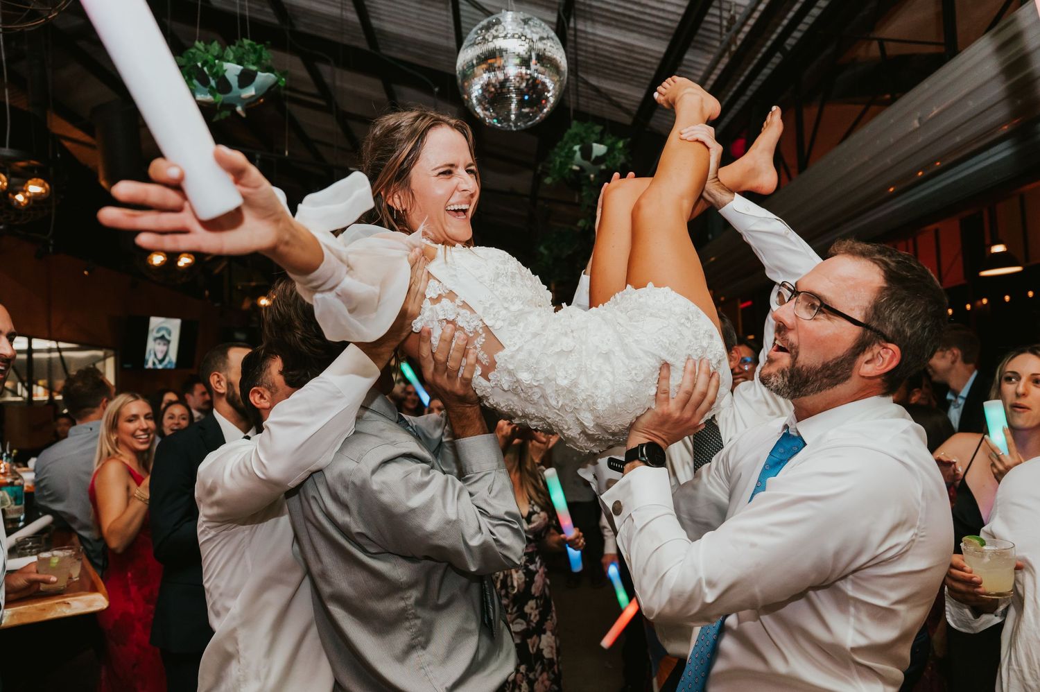 Wedding reception guests dancing and celebrating together on a crowded dance floor with raised arms and joyful expressions.
