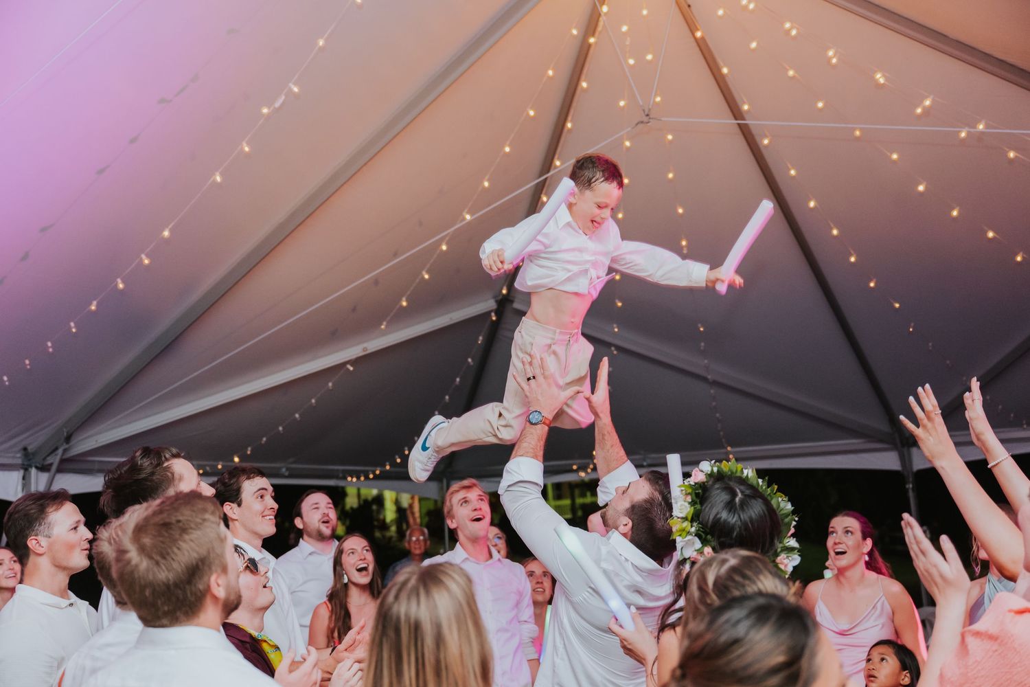 Wedding reception celebration under a tent with twinkling lights and guests dancing.