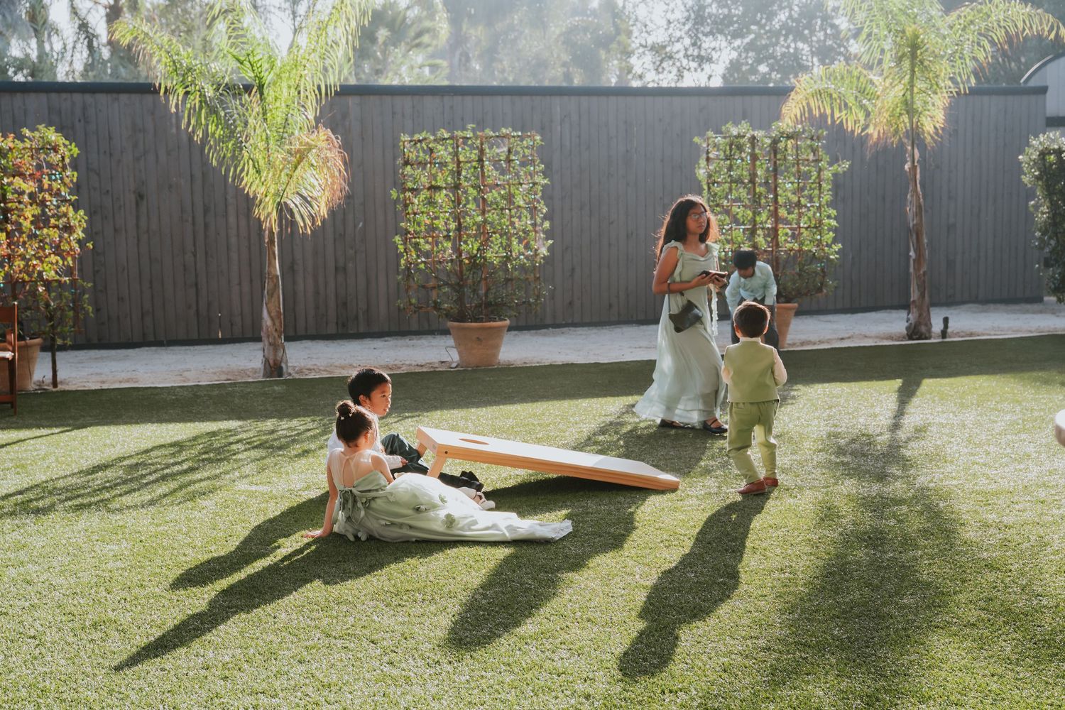 People enjoying a sunny day on artificial turf with palm trees and a modern fence in the background.