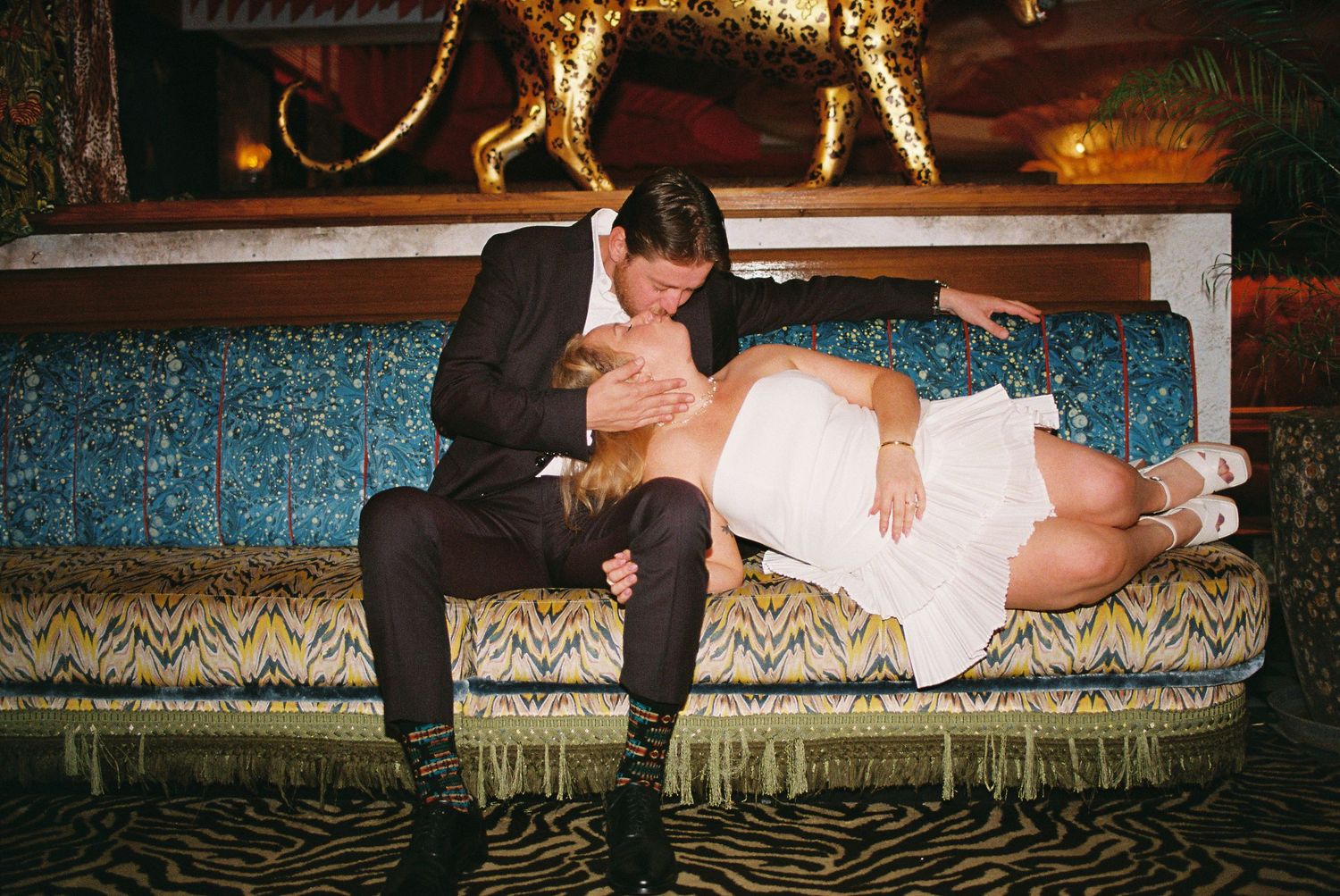 Couple sharing a romantic moment on a teal velvet sofa at a wedding reception venue.