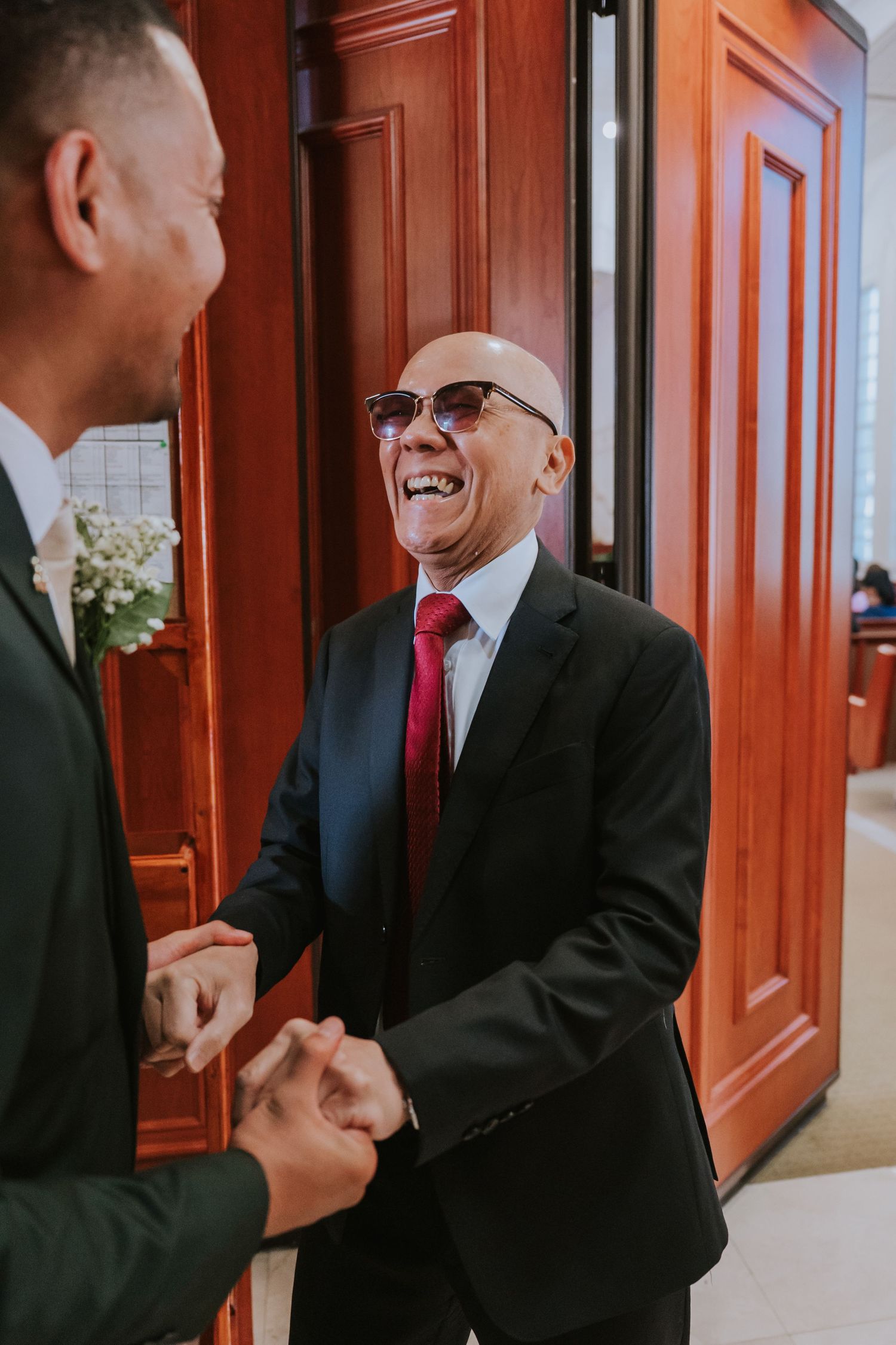 Two people in black suits and red ties having an animated conversation in a hallway with wooden paneled walls.