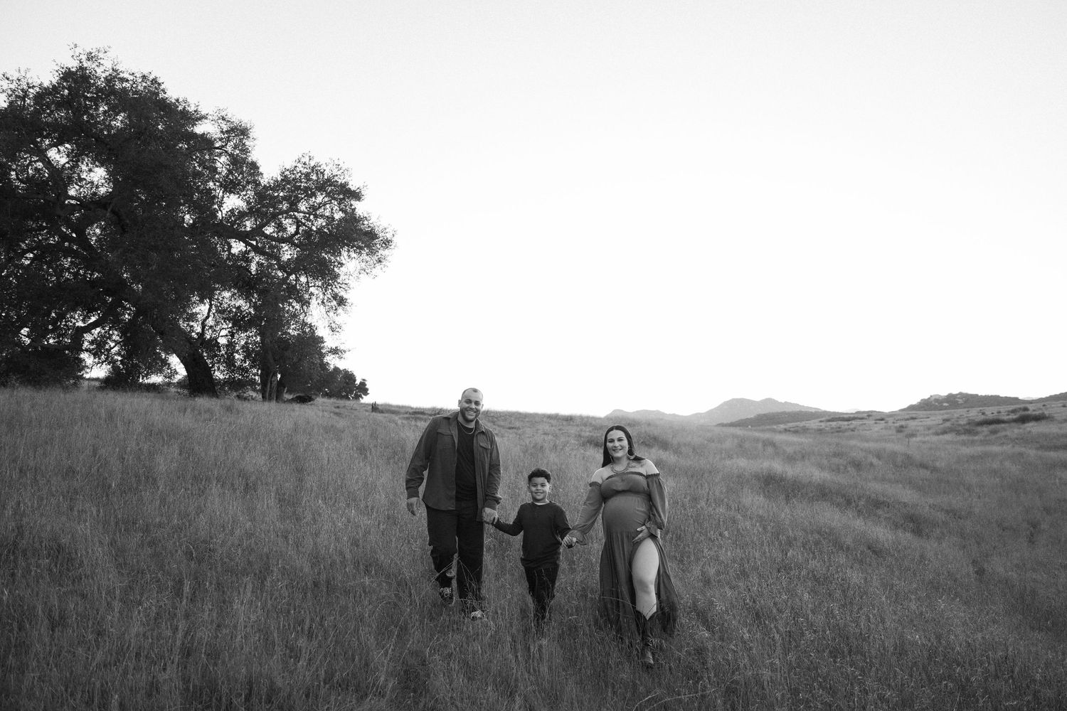 A black and white photo shows people walking together across a grassy hillside on a sunny day.