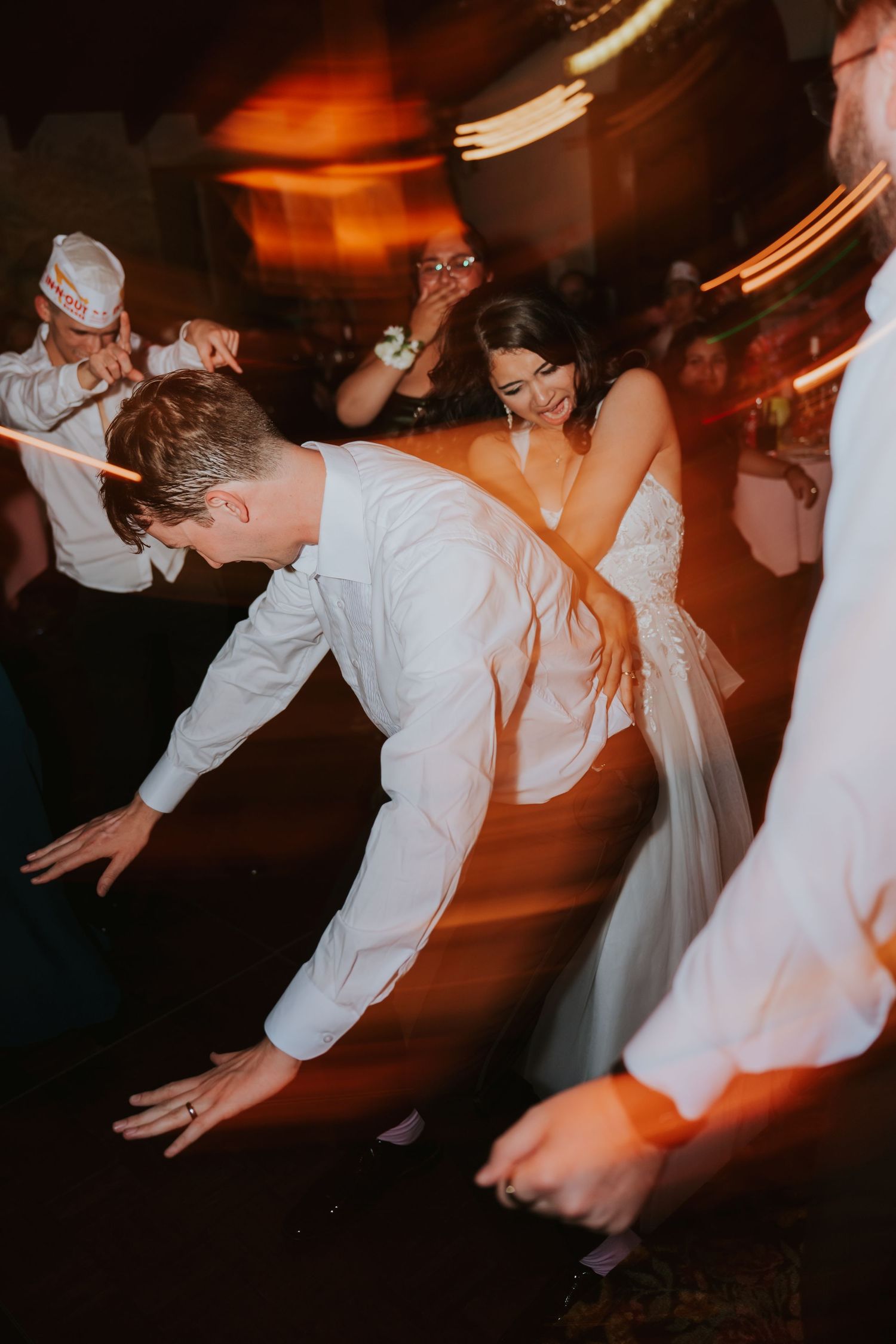 Wedding reception dance floor with energetic guests dancing in motion blur under warm lighting.